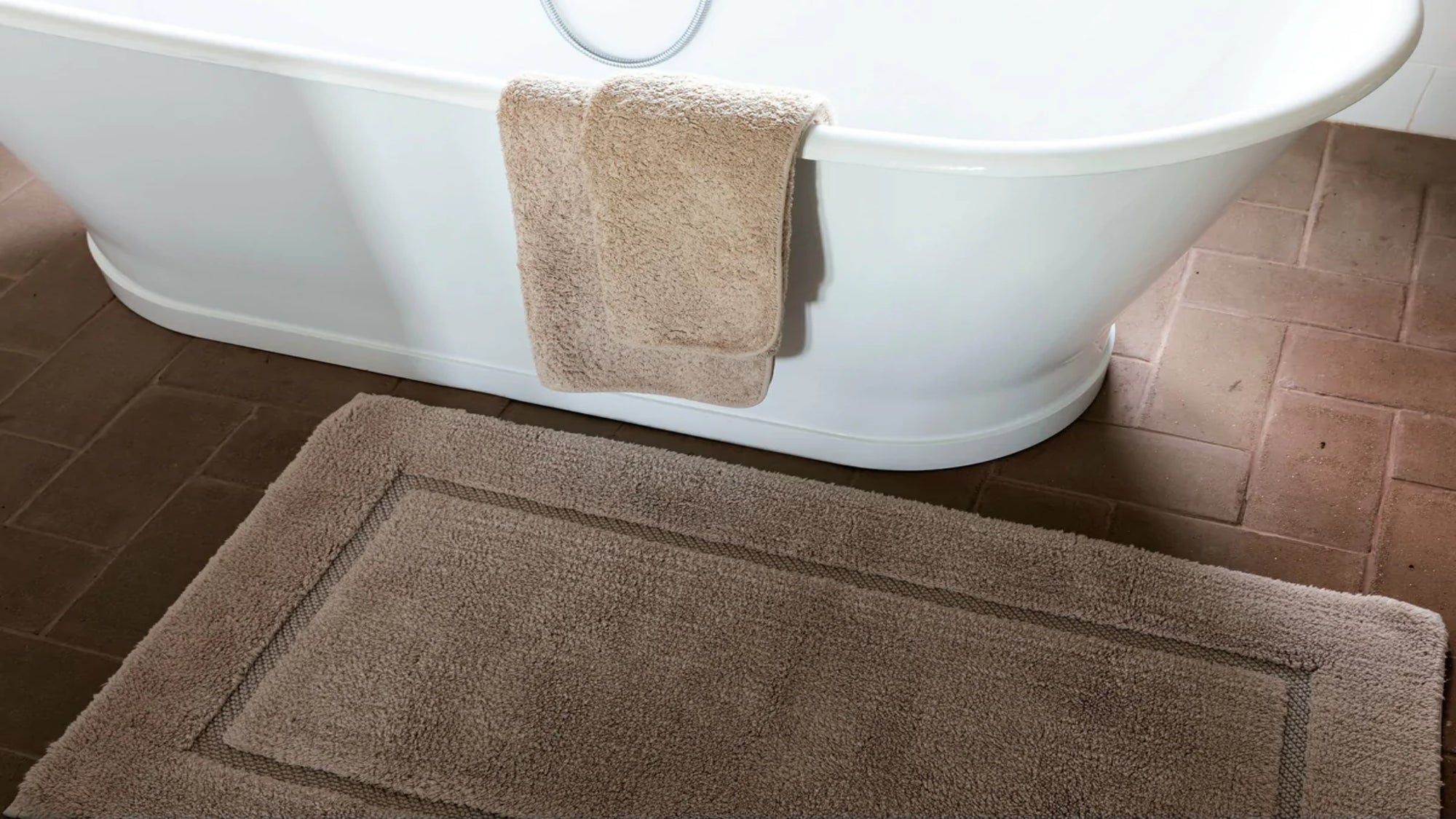 Brown bath rug on bathroom floor beside a tub