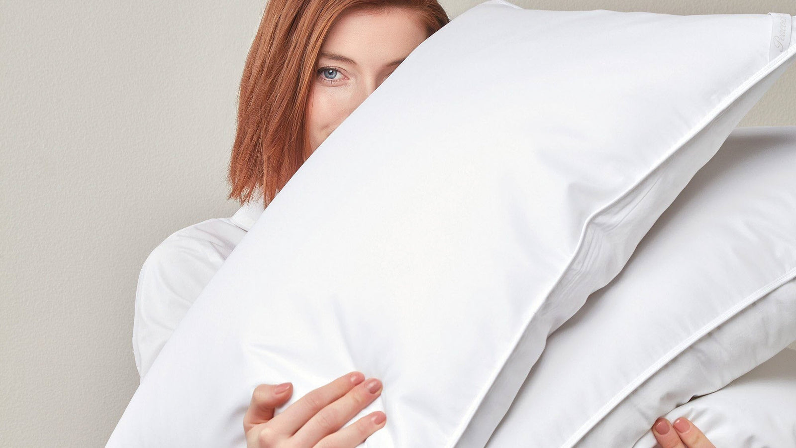 Person holding a large white pillow against a plain background