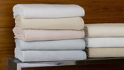 SFERRA Luxury Blanket Buyer's Guide: Comparing St. Moritz, Nerino, Olindo, and Savoy blankets Piled Folded Towels on Metal Bench Fine Linens