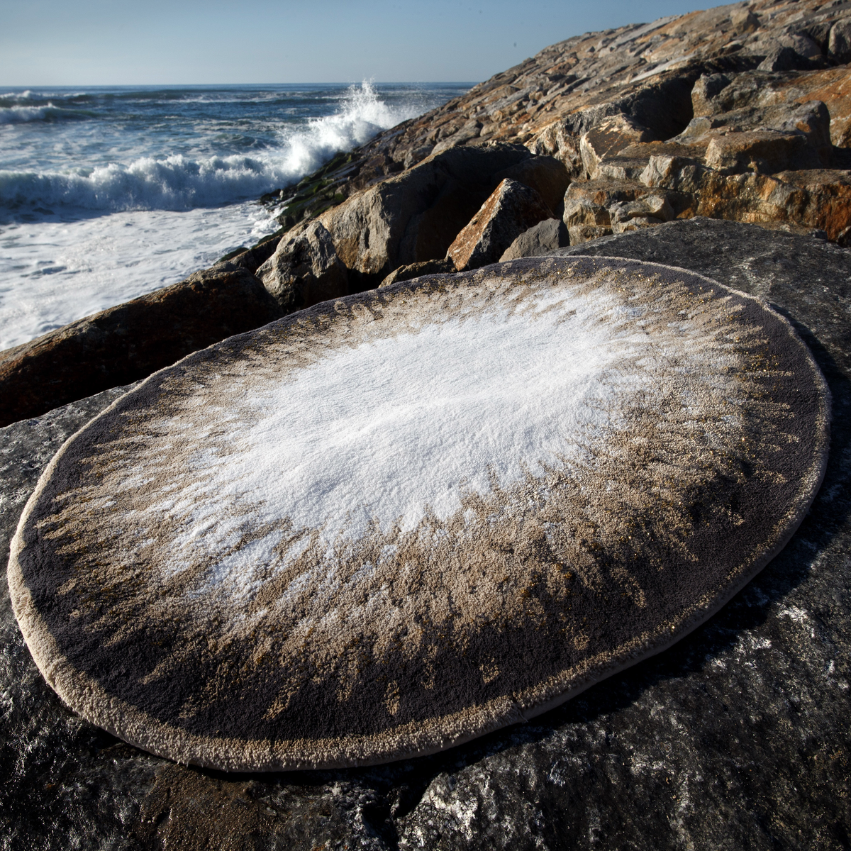 Taupe colored Abyss Habidecor Atom Bath Rug placed on a rock outdoors