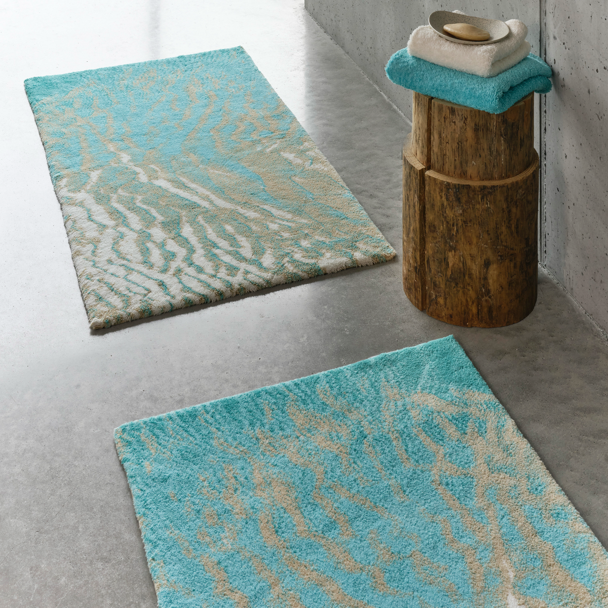 Two Turquoise colored Abyss Habidecor Beach Bath Rugs on concrete floor