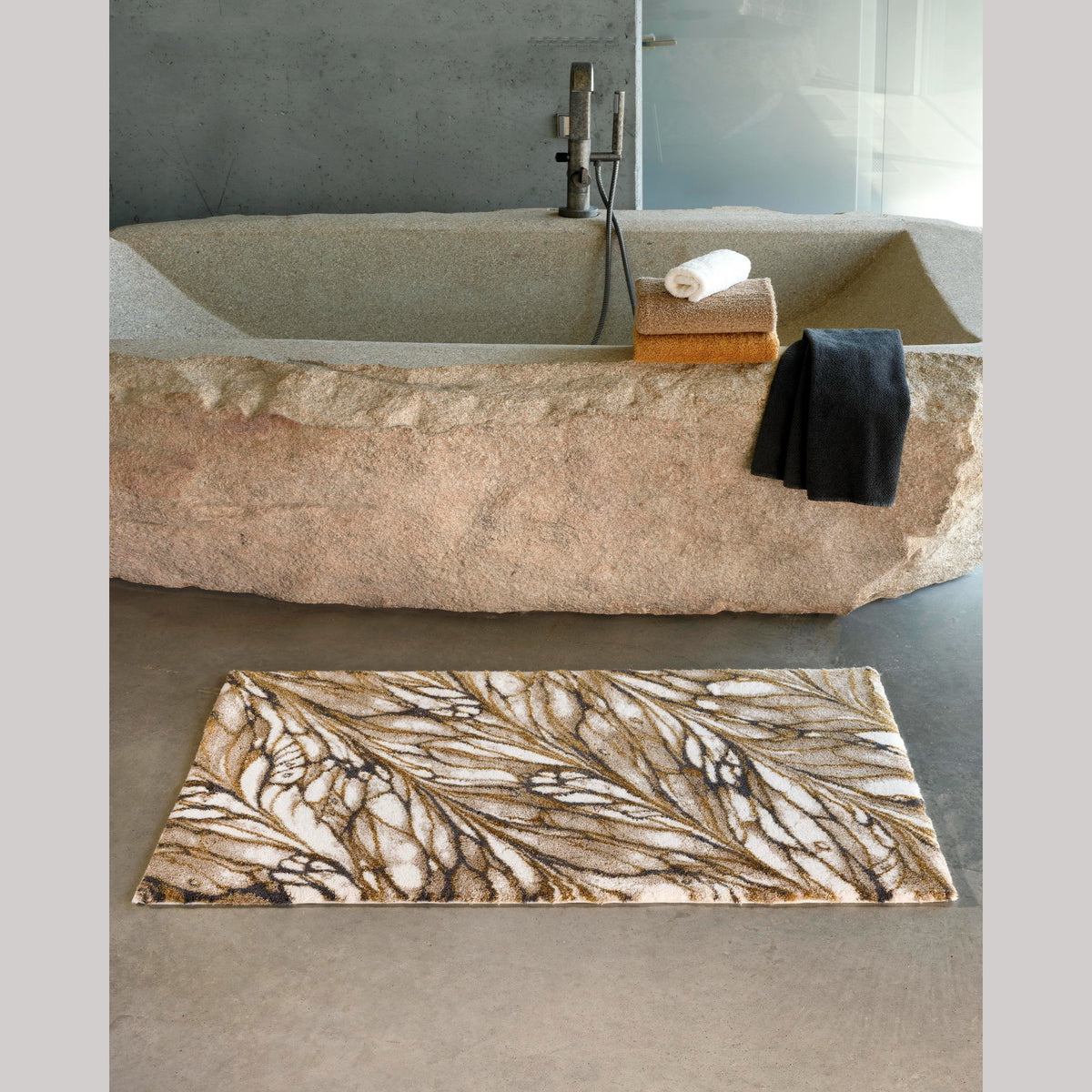 Gold Abyss Habidecor Diane Bath Rug beside stone bath tub