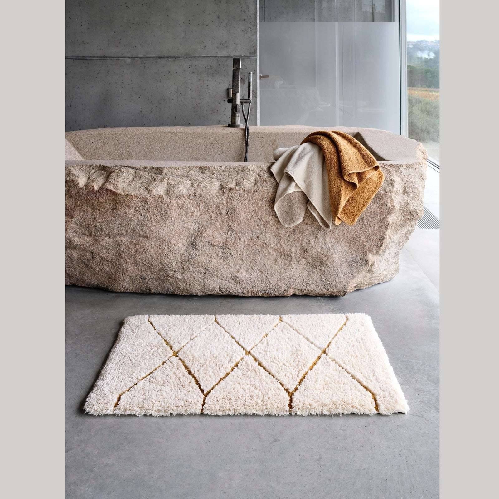 Gold Abyss Habidecor Heritage Bath Rug beside a bath tub