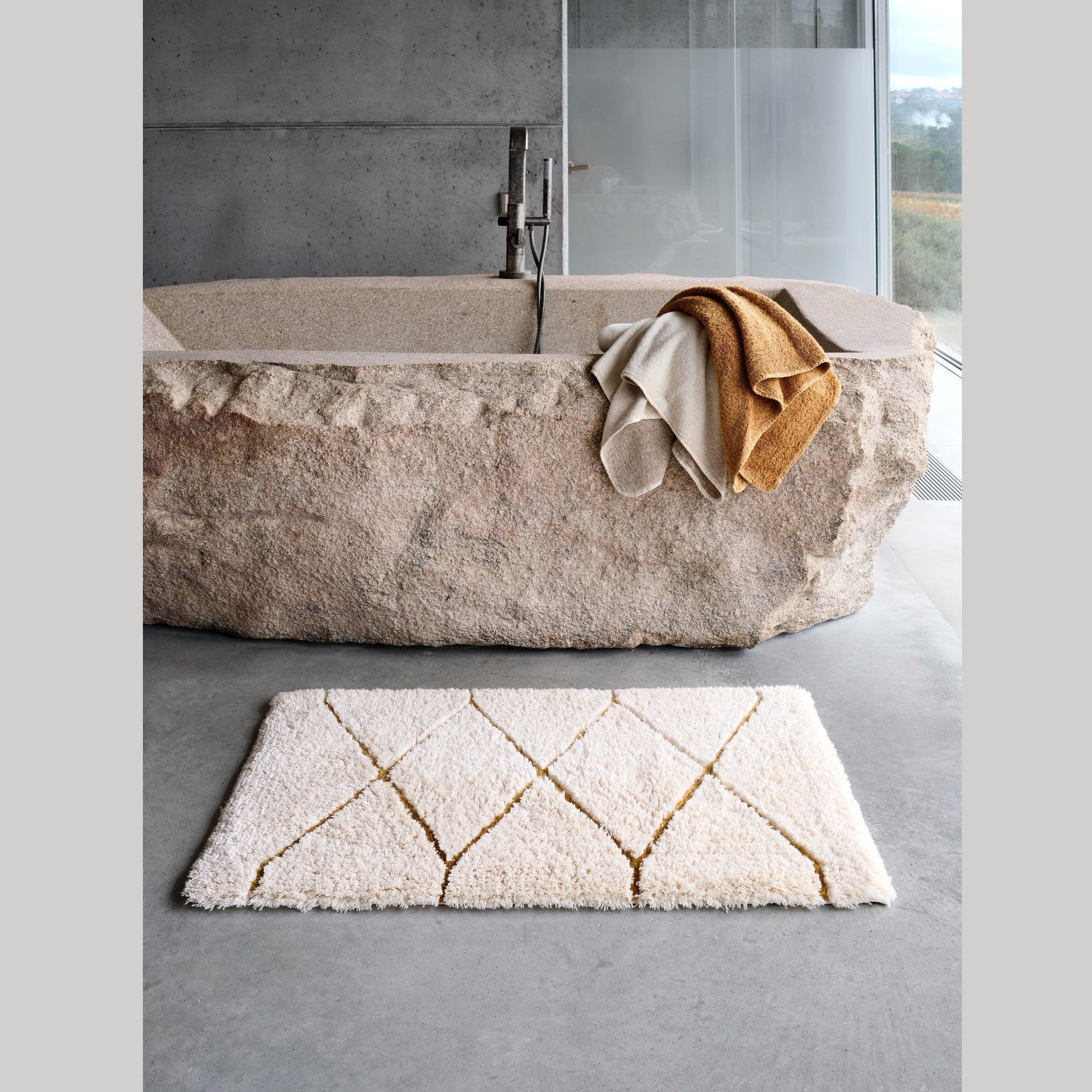 Gold Abyss Habidecor Heritage Bath Rug beside a bath tub