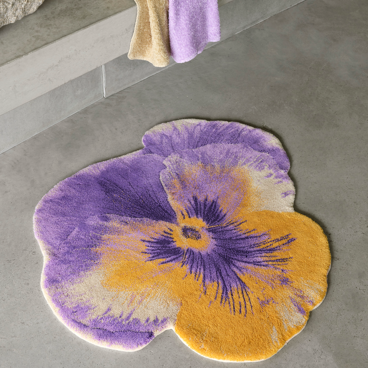 The Abyss Habidecor Pansy Bath Rug, crafted from Egyptian cotton, brightens a gray concrete floor near a low bench with towels