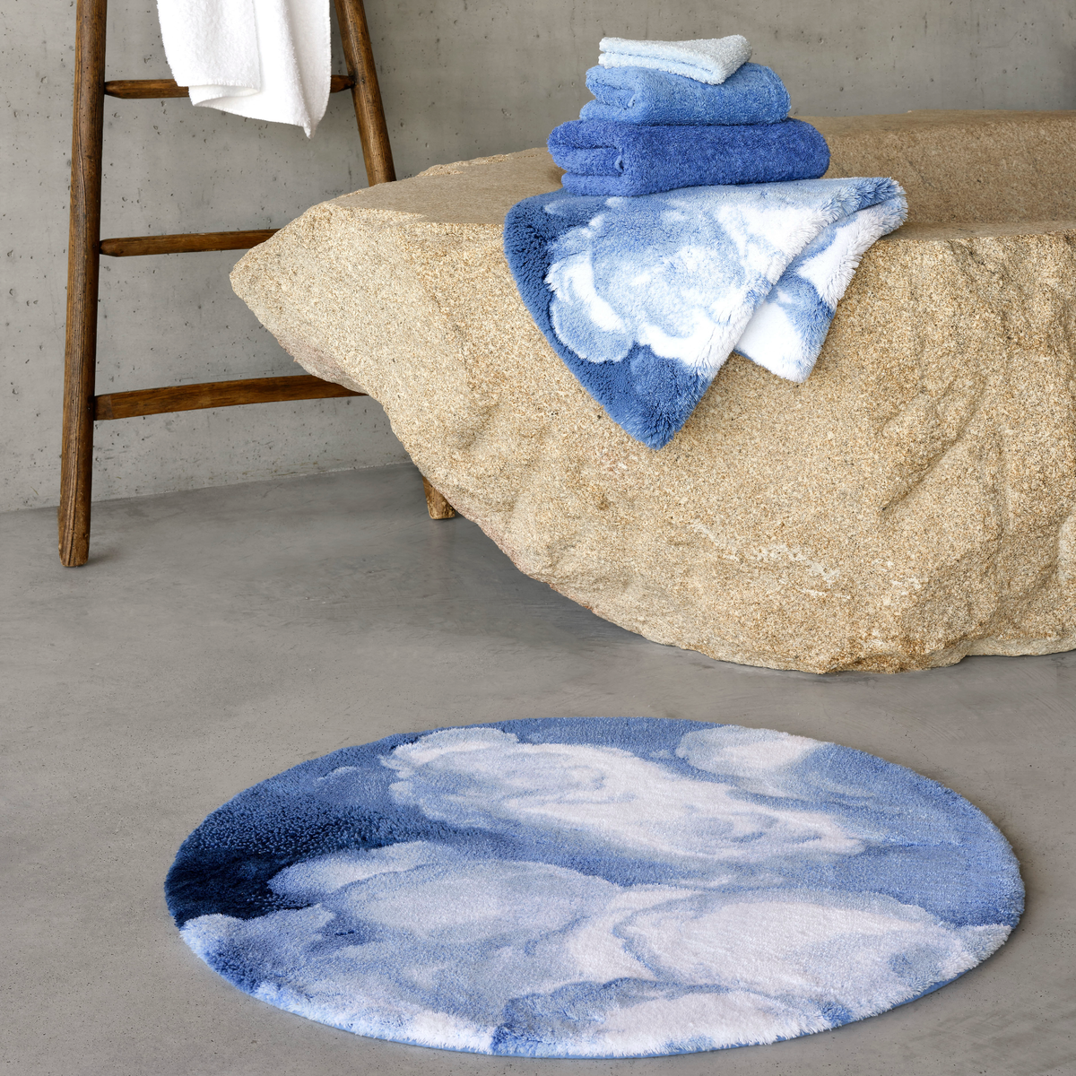 A Regatta colored Abyss Habidecor Walker Bath Rug on concrete beside a stone tub with stacked matching towels