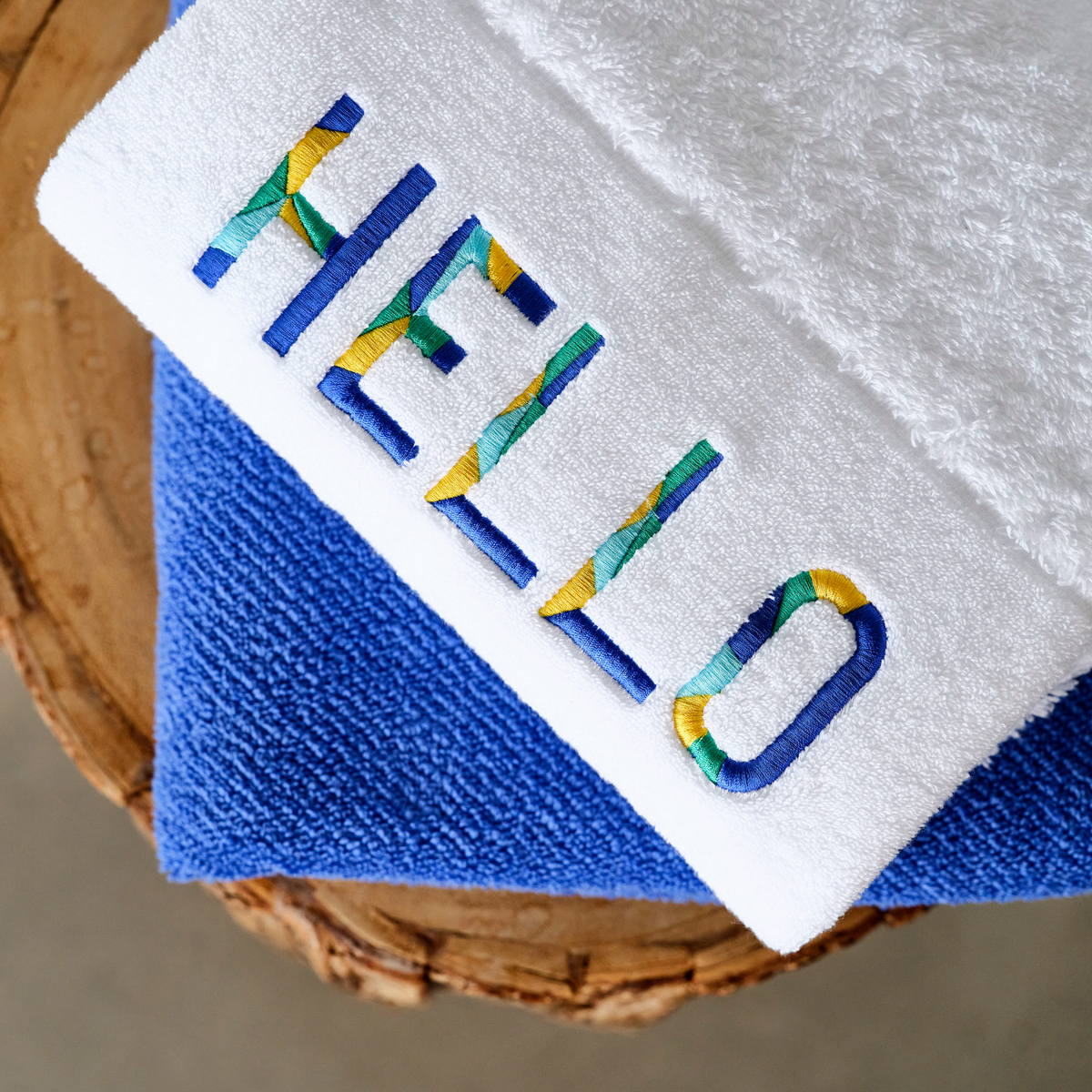 Abyss Hello Embroidered Bath Towels in Marina (304) color rests atop a folded blue Egyptian Giza cotton towel on wood