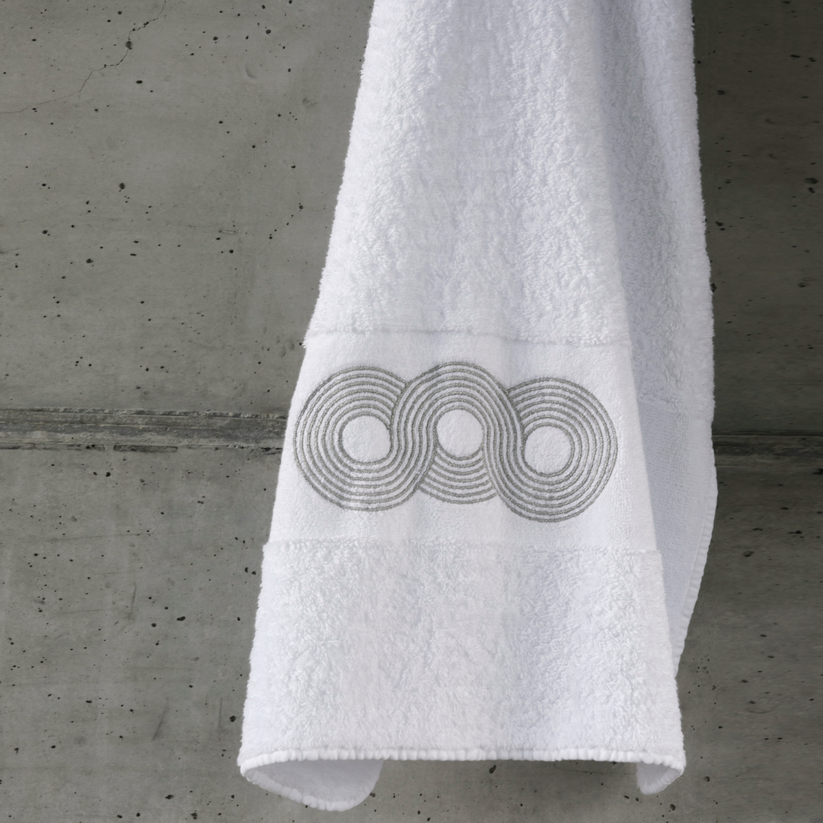 A luxury towel with a geometric circular pattern hangs against a concrete wall.