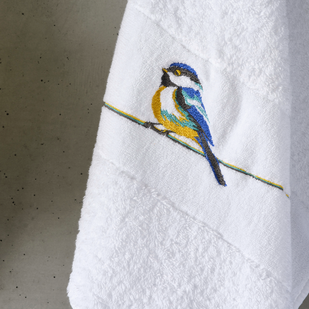 White embroidered bird towel crafted from luxurious Egyptian Giza cotton, featuring a colorful bird on a yellow line.