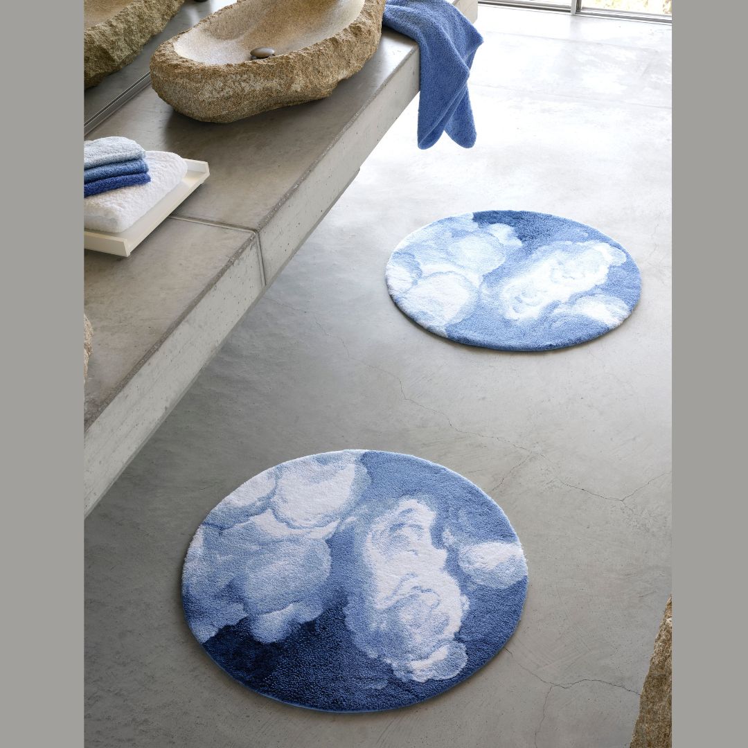 Two round plush absorbent bath rugs with cloud patterns sit on a concrete floor near stone and concrete surfaces.