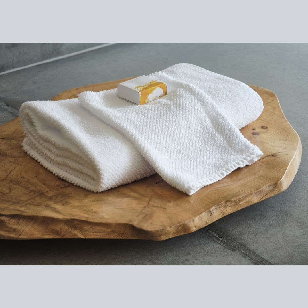 A folded Abyss Twill Bath Towel and soap rest on a natural wood slab atop a gray stone surface.