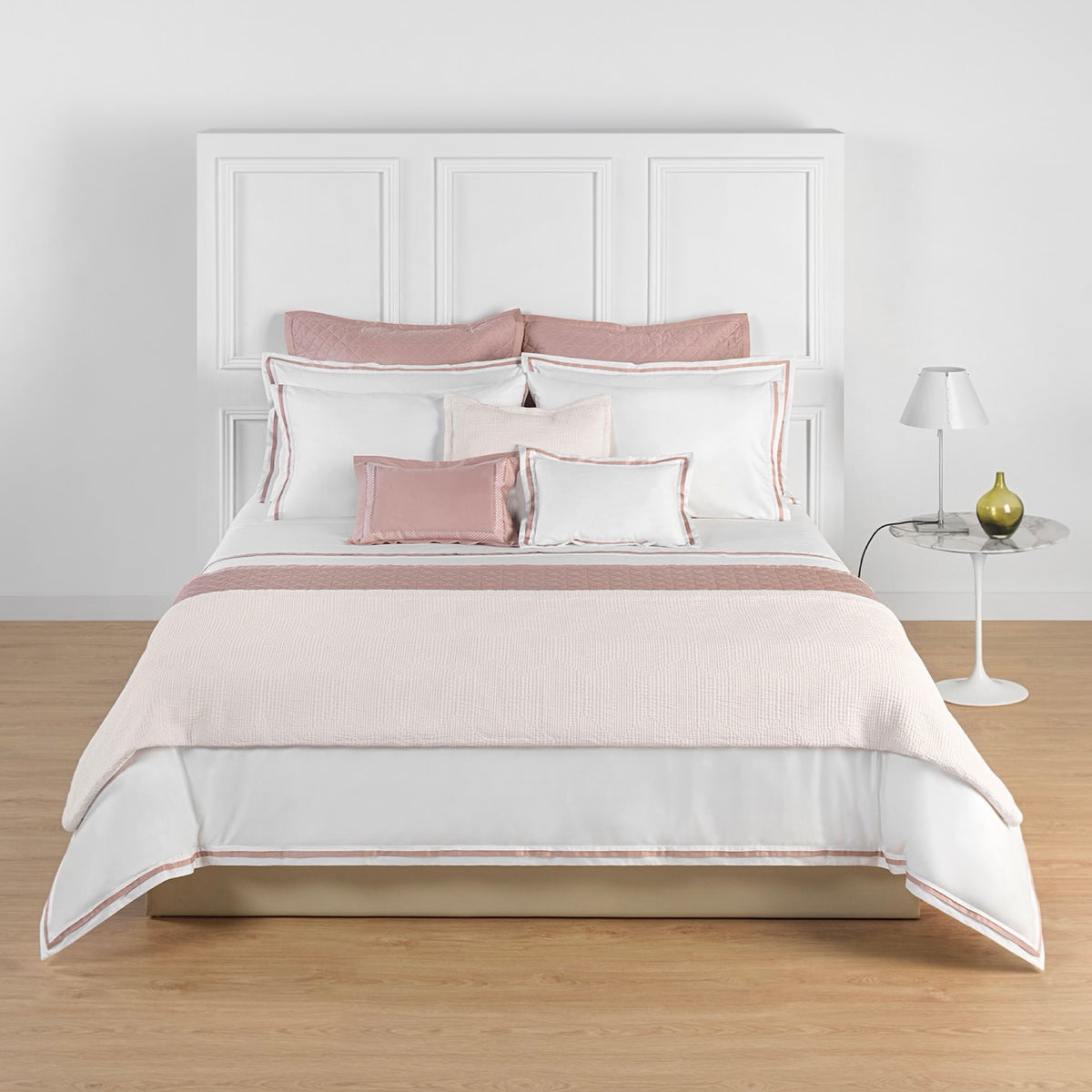 Bed with luxury Charm Pink Amalia Eden Sea Island Cotton Bedding, and a side table with a lamp and glass vase.