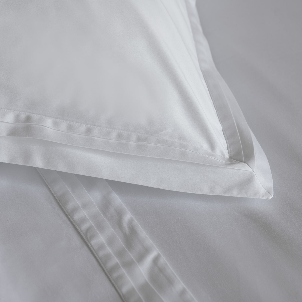 Corner of White 750 thread count pillowcase from Amalia Eden Sea Island Cotton Bedding collection resting on a matching flat sheet