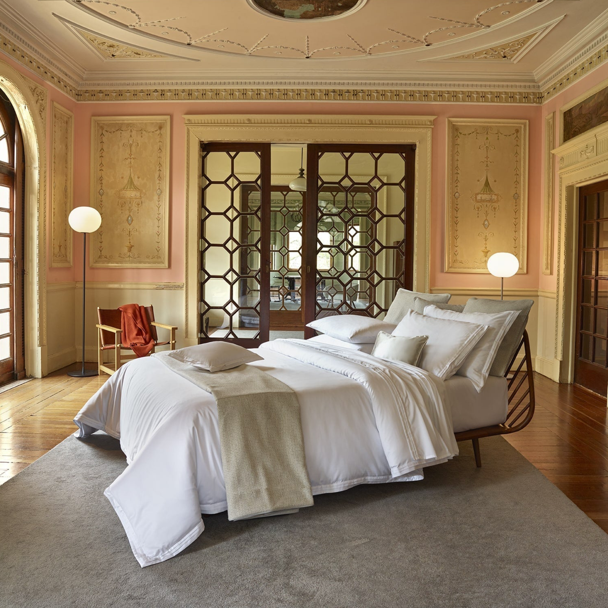 A made bed with 750 thread count White Amalia Eden Sea Island Cotton Bedding and a runner in a room with a decorative ceiling and wooden room divider