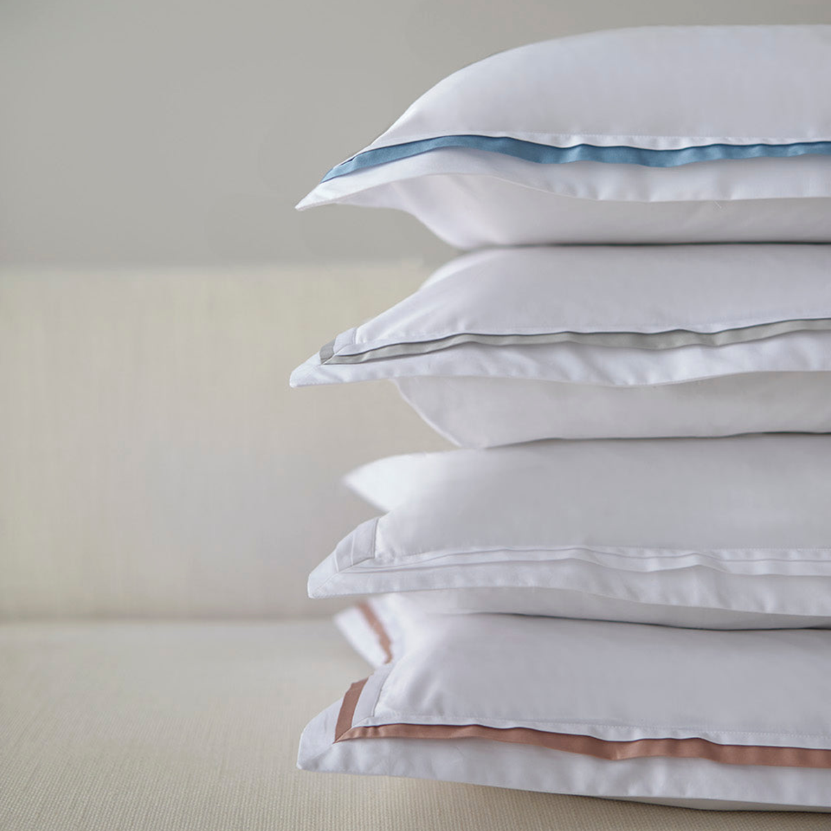 A vertical stack of Amalia Eden Sea Island Cotton Shams in White, Cool Grey, Tivoli and Cham Pink trim colors