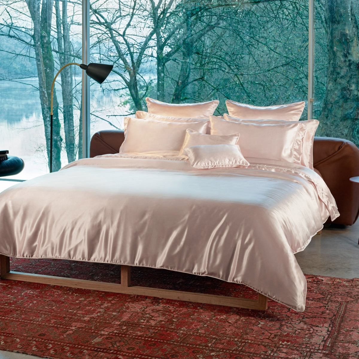 Bed with Pink Amalia Maria Mulberry Silk Bedding, set on a red patterned rug before a window