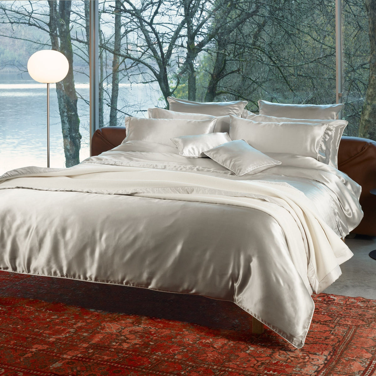Bed with Silver Amalia Maria Mulberry Silk Bedding, set on a red patterned rug before a window