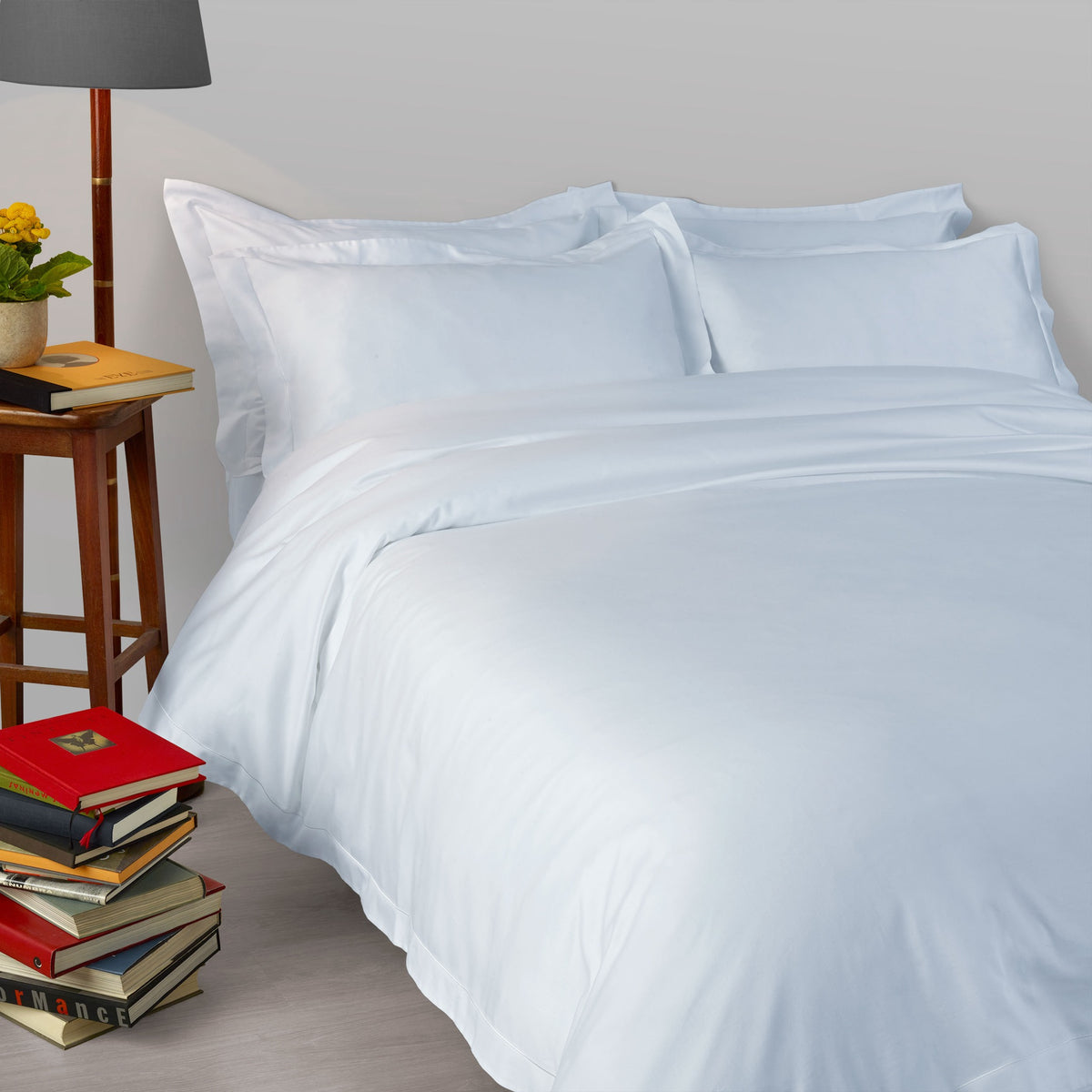 A bed made with 430 thread count Pale Blue Amalia Suave Giza 94 Bedding, next to a lamp