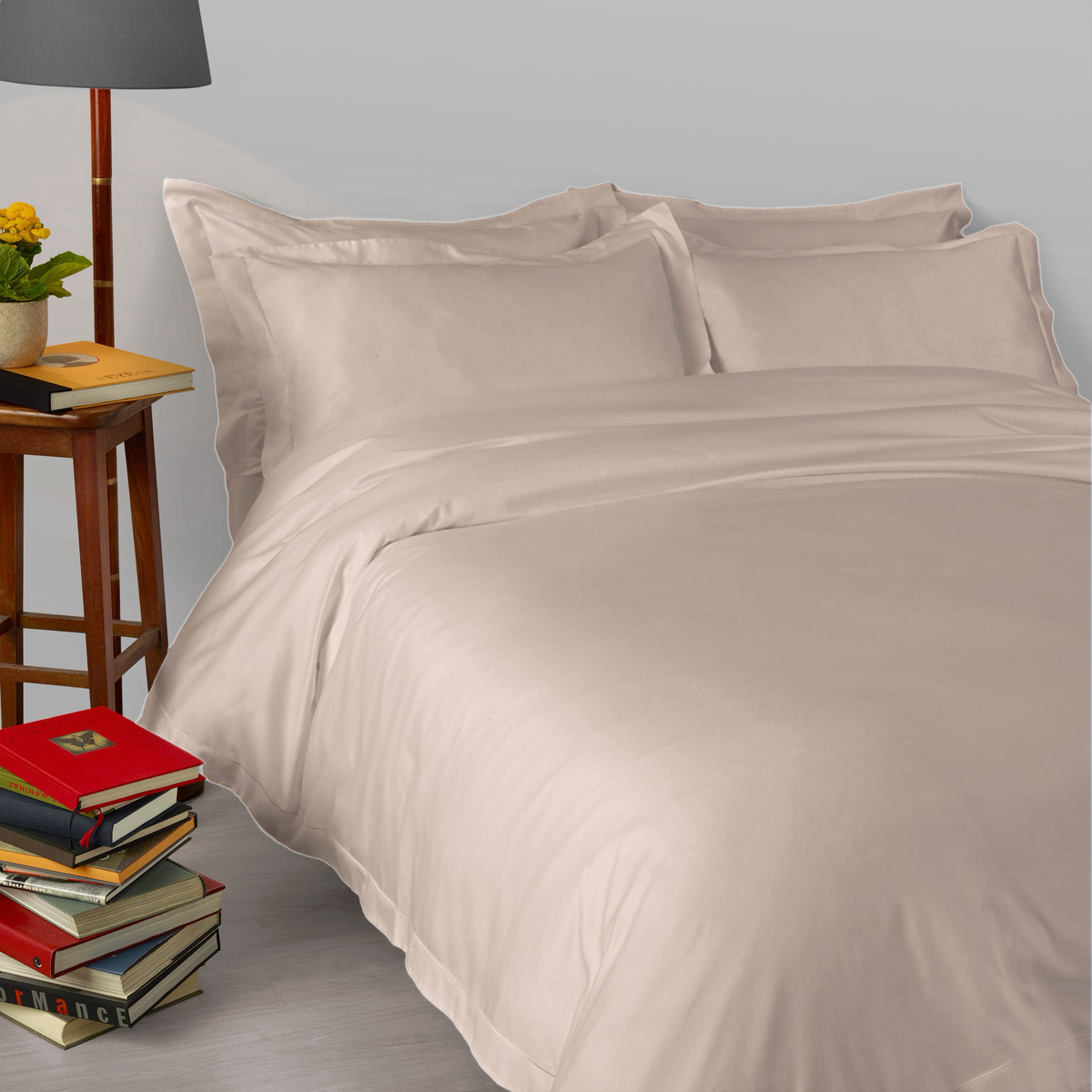 A bed made with 430 thread count Tiramisu Amalia Suave Giza 94 Bedding, next to a stack of books with a lamp
