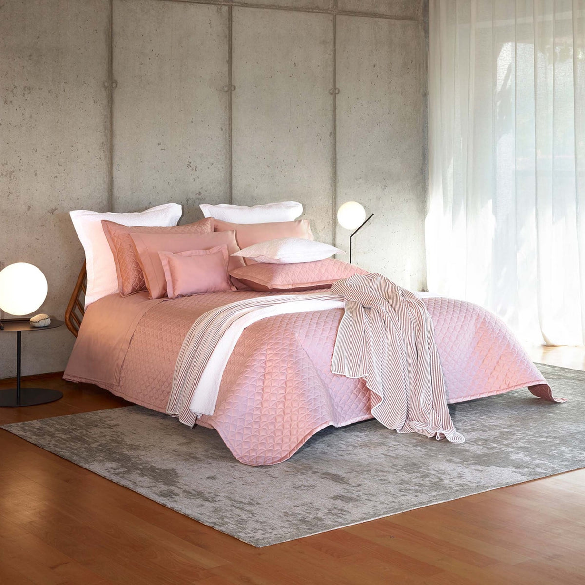 A bed in a well lit room with Charm Pink Amalia Suave Quilted Bedding