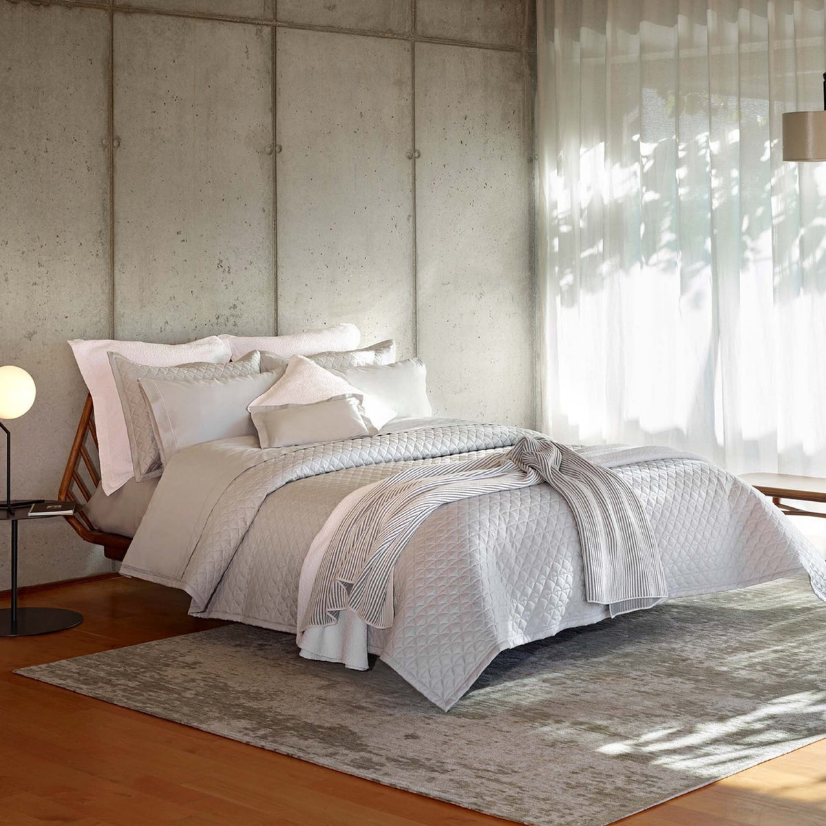 A bed in a well lit room with Cool Grey Amalia Suave Quilted Bedding