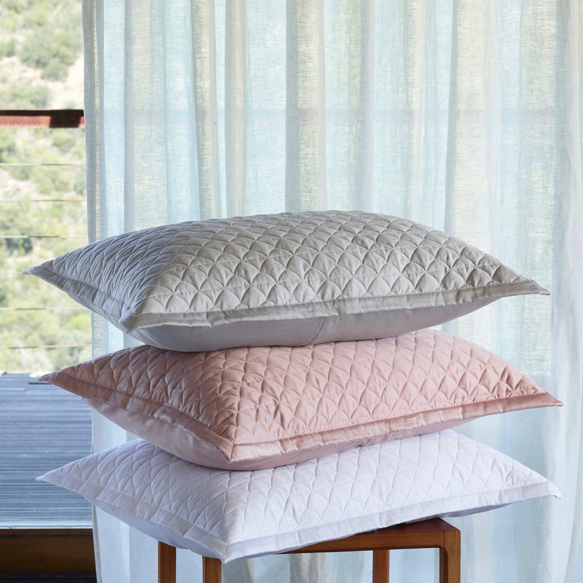 A stack of Amalia Suave Quilted Pillows in White, Charm Pink, Cool Grey colors