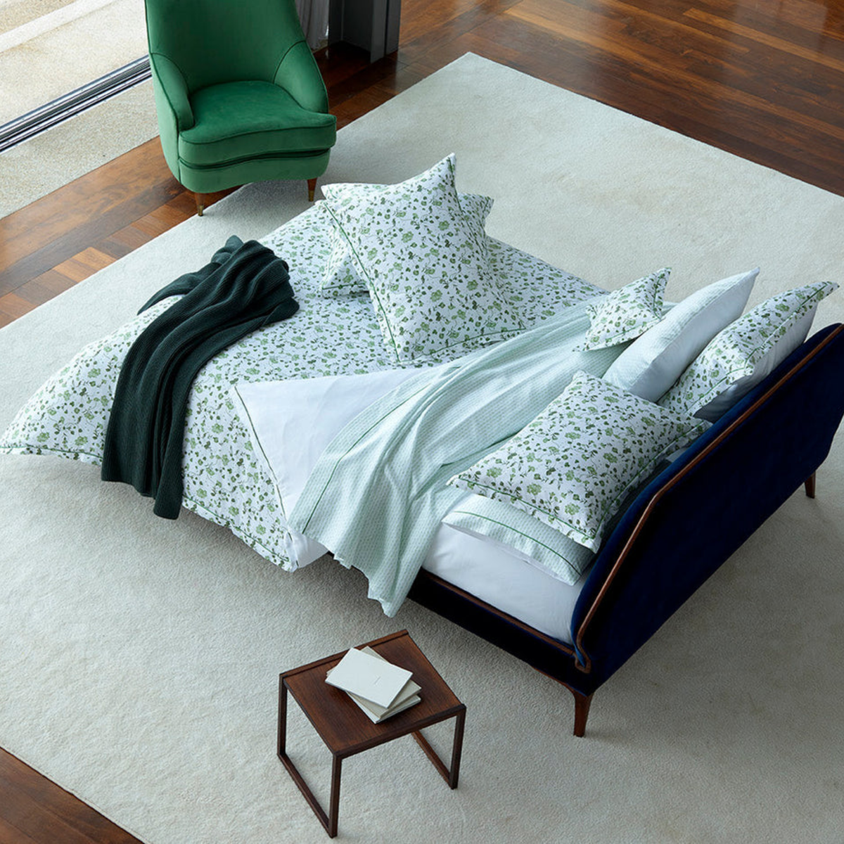 A bed with Primavera Amalia Vila-Flor Bedding, next to a velvet armchair and a small table