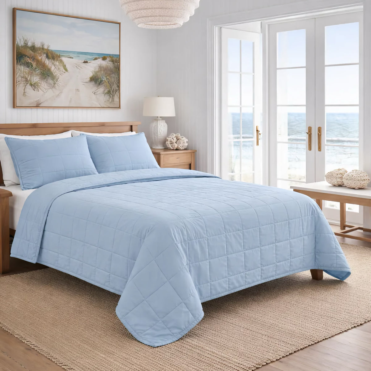 A neatly made bed with Powder Blue colored Ann Gish Cotton Canvas Coverlet Set in a bright room and an ocean view through a large window