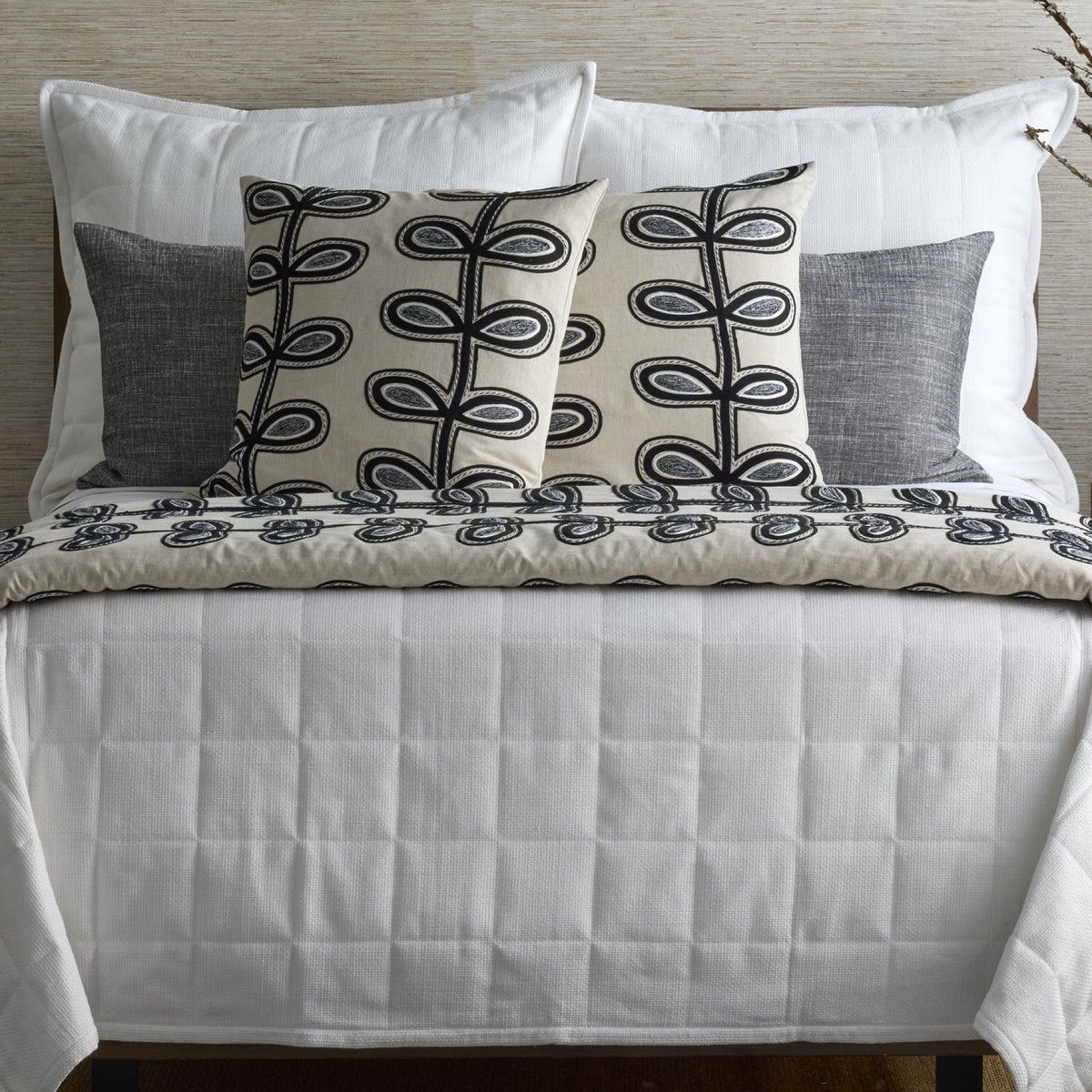 A neatly made bed with white bedding, and two Ann Gish Fellini Decorative Pillows in Natural and Charcoal colors