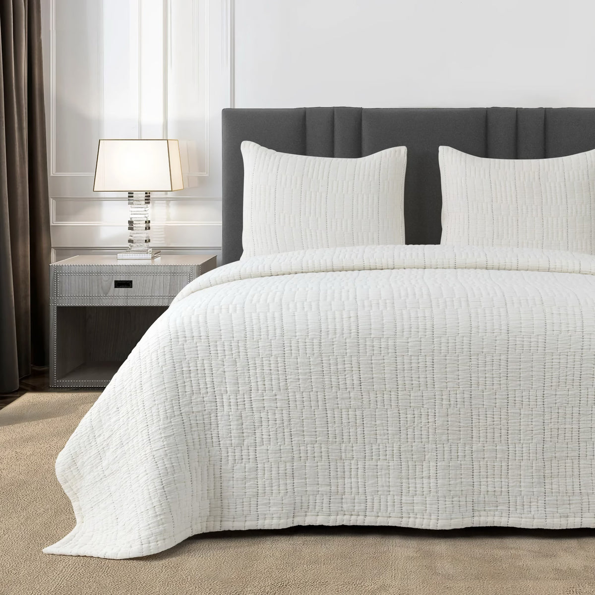 A neatly made bed with a Bone colored Ann Gish Pickstitch Coverlet Set in a modern bedroom