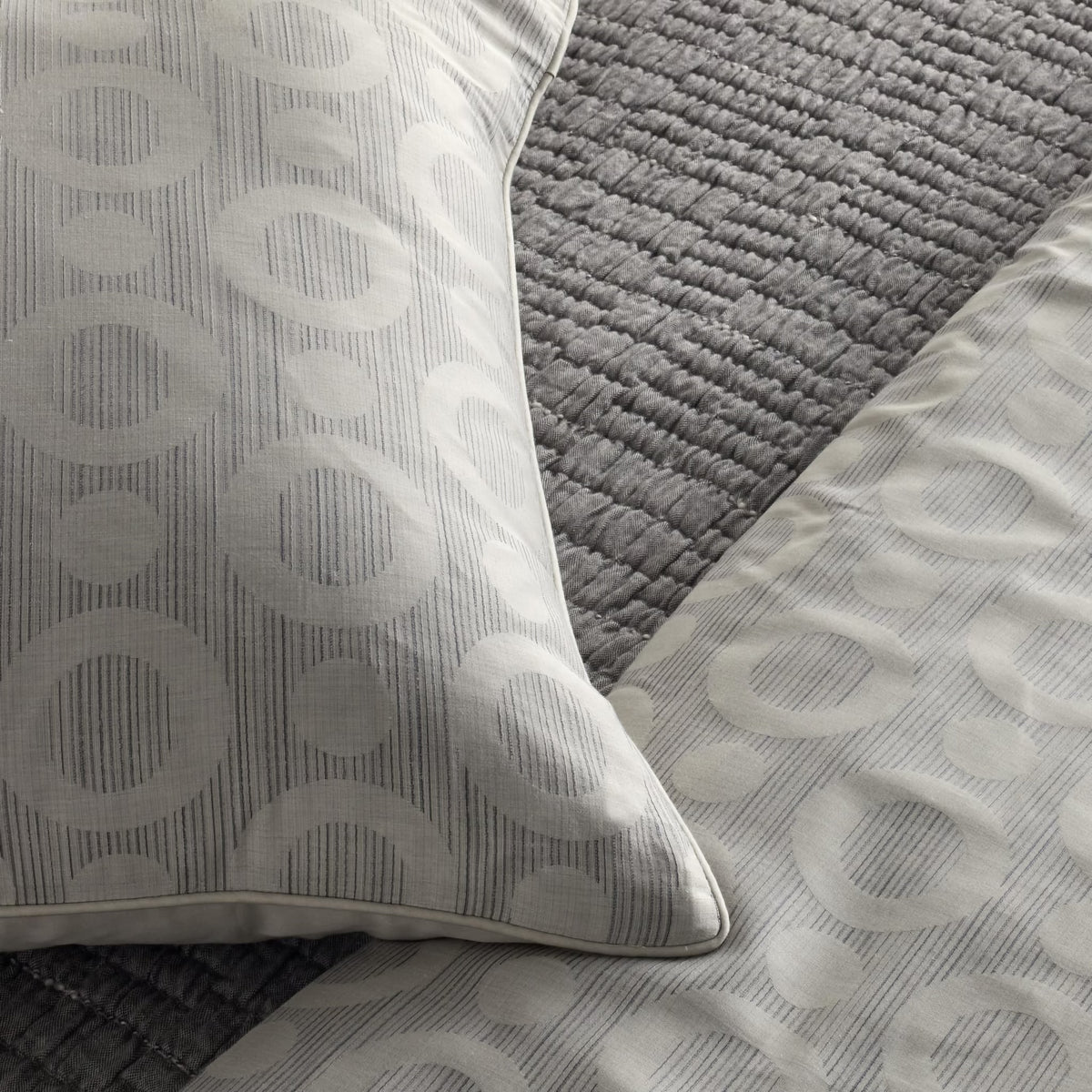 Close-up of a bed with a Charcoal colored Ann Gish Pickstitch Coverlet and pillows featuring a light gray circular pattern