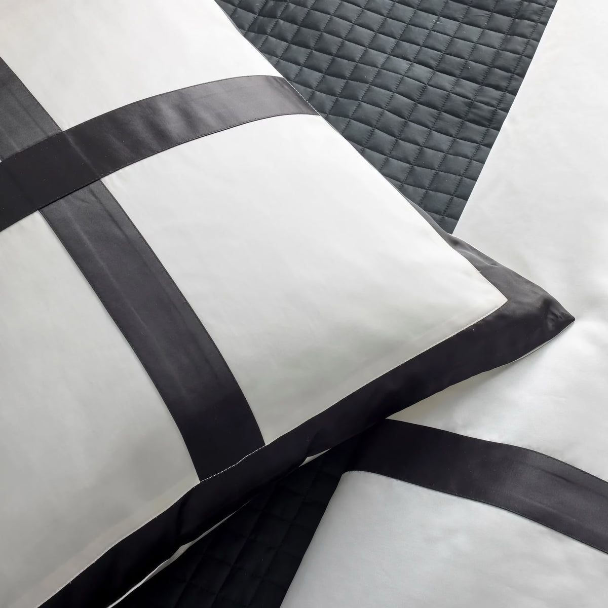White pillows with black satin bands, atop a dark Ann Gish quilted coverlet, create a striking luxury bedding set.