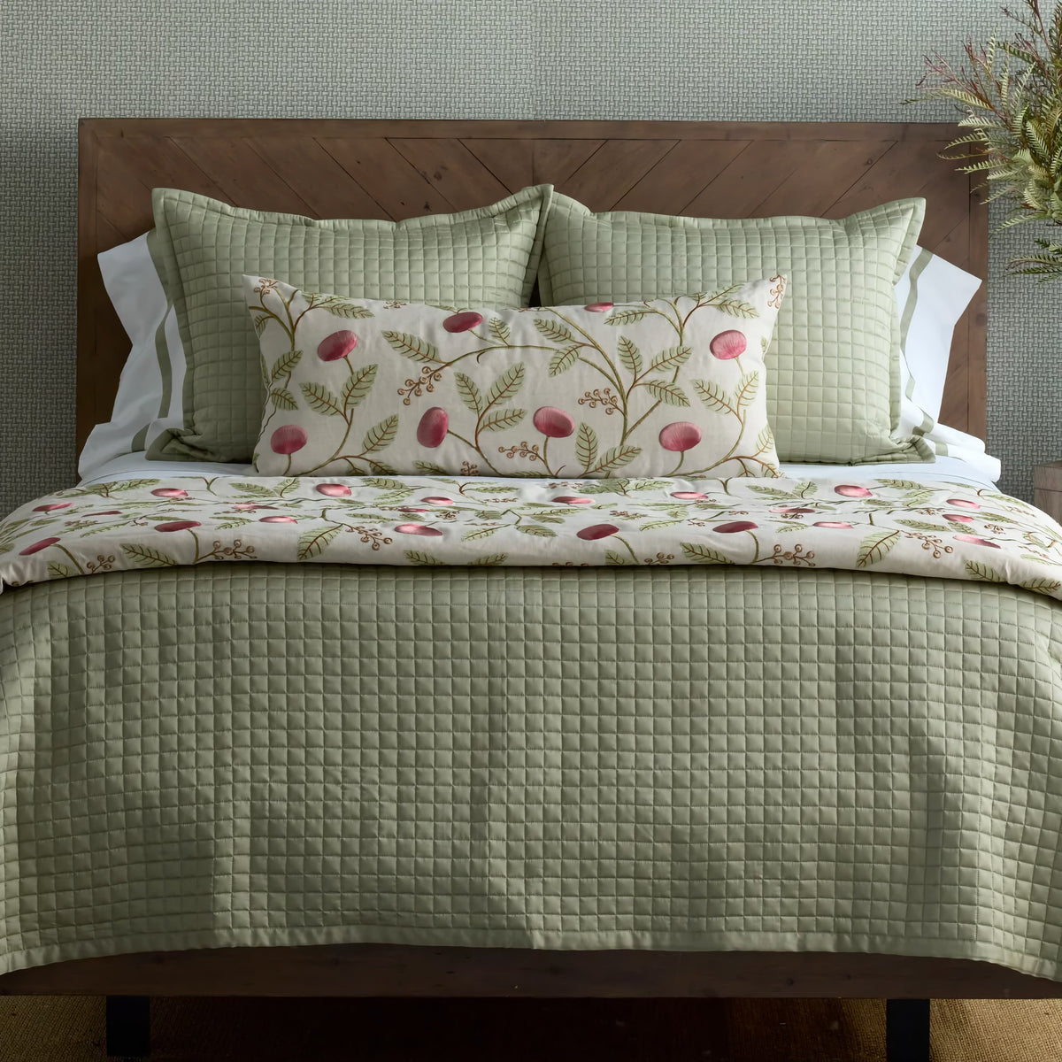 A bed with a green Lyocell fabric comforter, matching pillows, and a floral accent against a wood headboard.