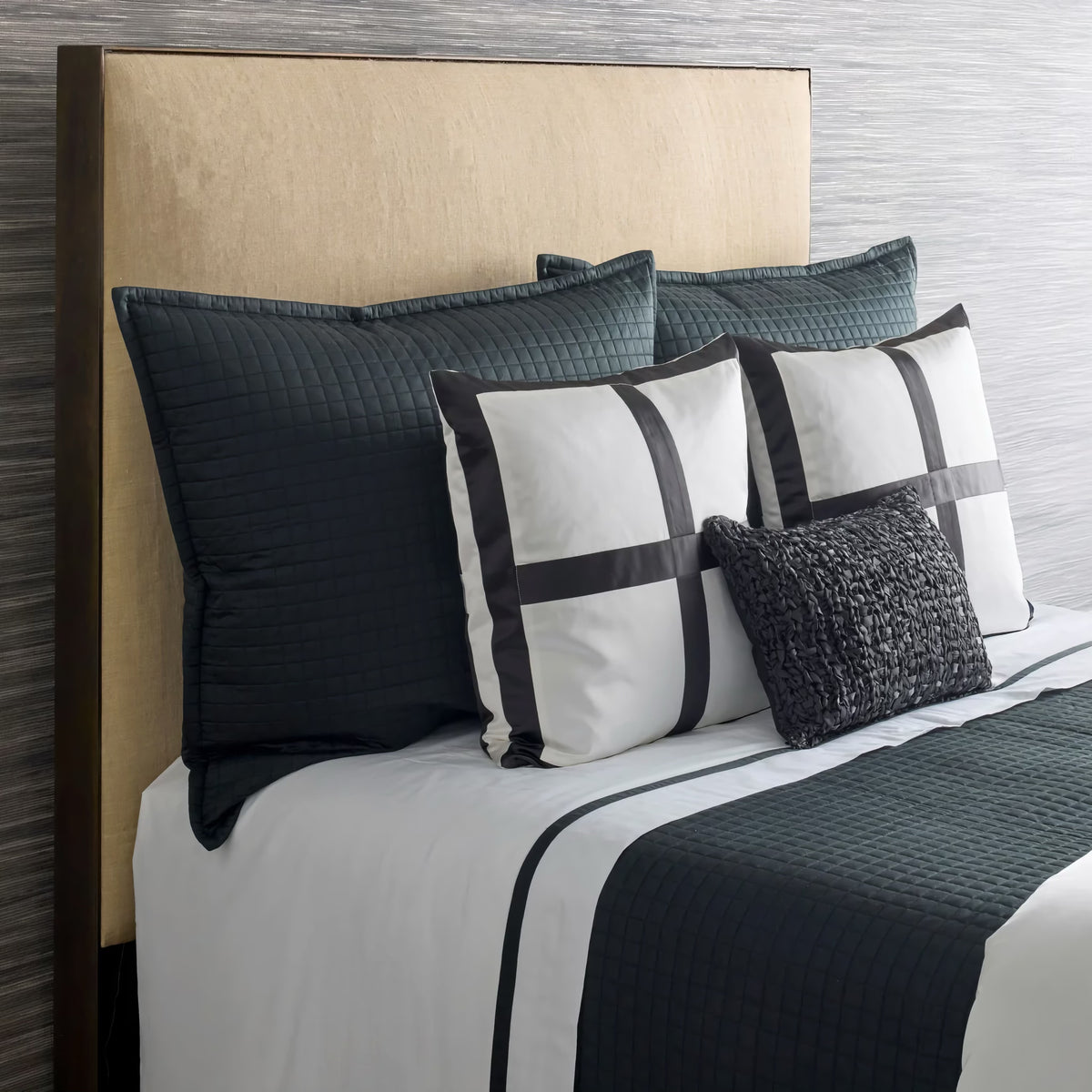 Bed with a beige headboard, luxury bedding set, black and white linens, and an Ann Gish quilted coverlet.