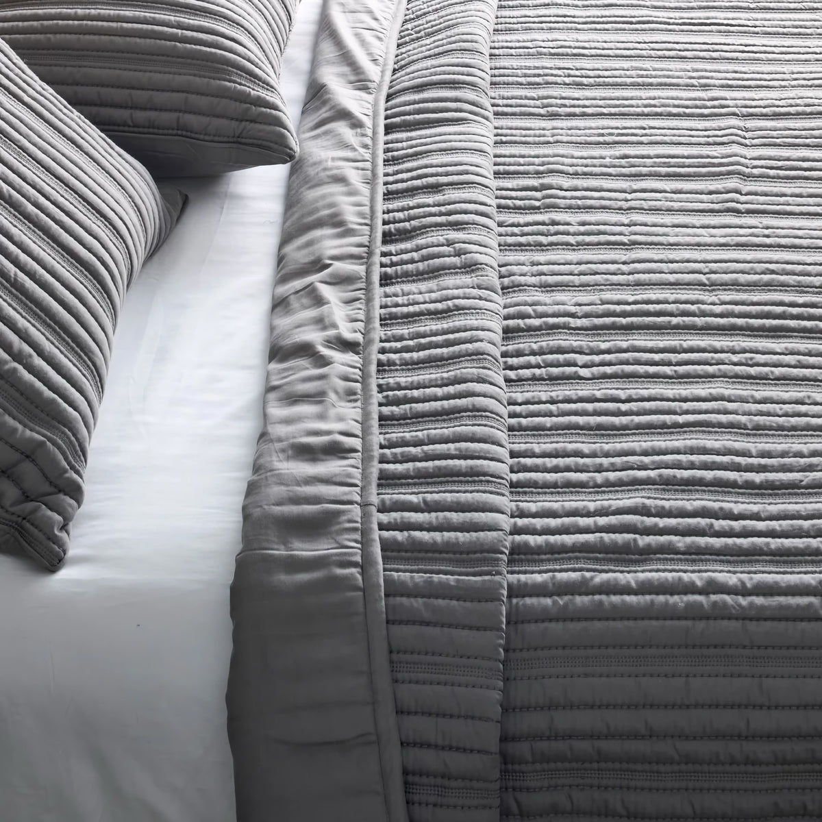 Close-up of a neatly made bed with gray striped modern bedding and two matching pillows on white sheets.