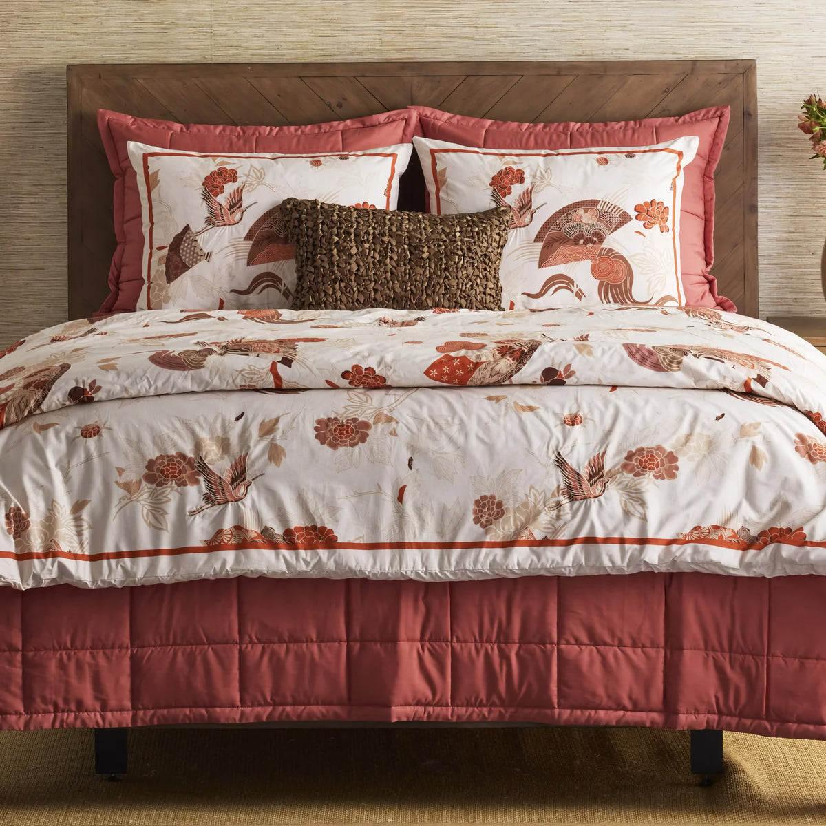 Bed with a wooden headboard, floral and bird-patterned bedding, and a Persimmon colored Ann Gish Slub Tencel Quilted Coverlet Set