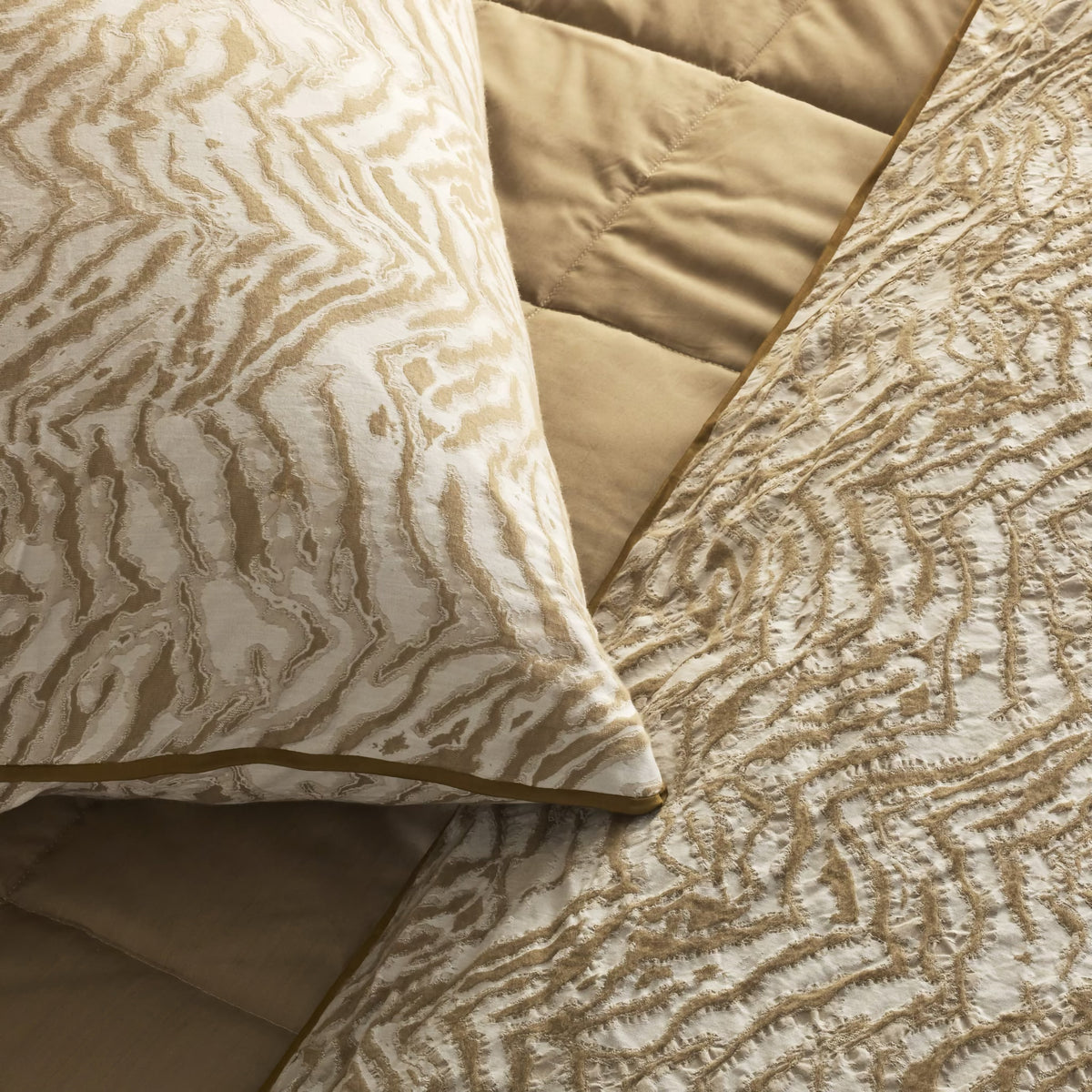 A close-up of a bed with an Cafe au Lait colored Ann Gish Slub Tencel Quilted Coverlet Set and matching wavy-patterned pillow