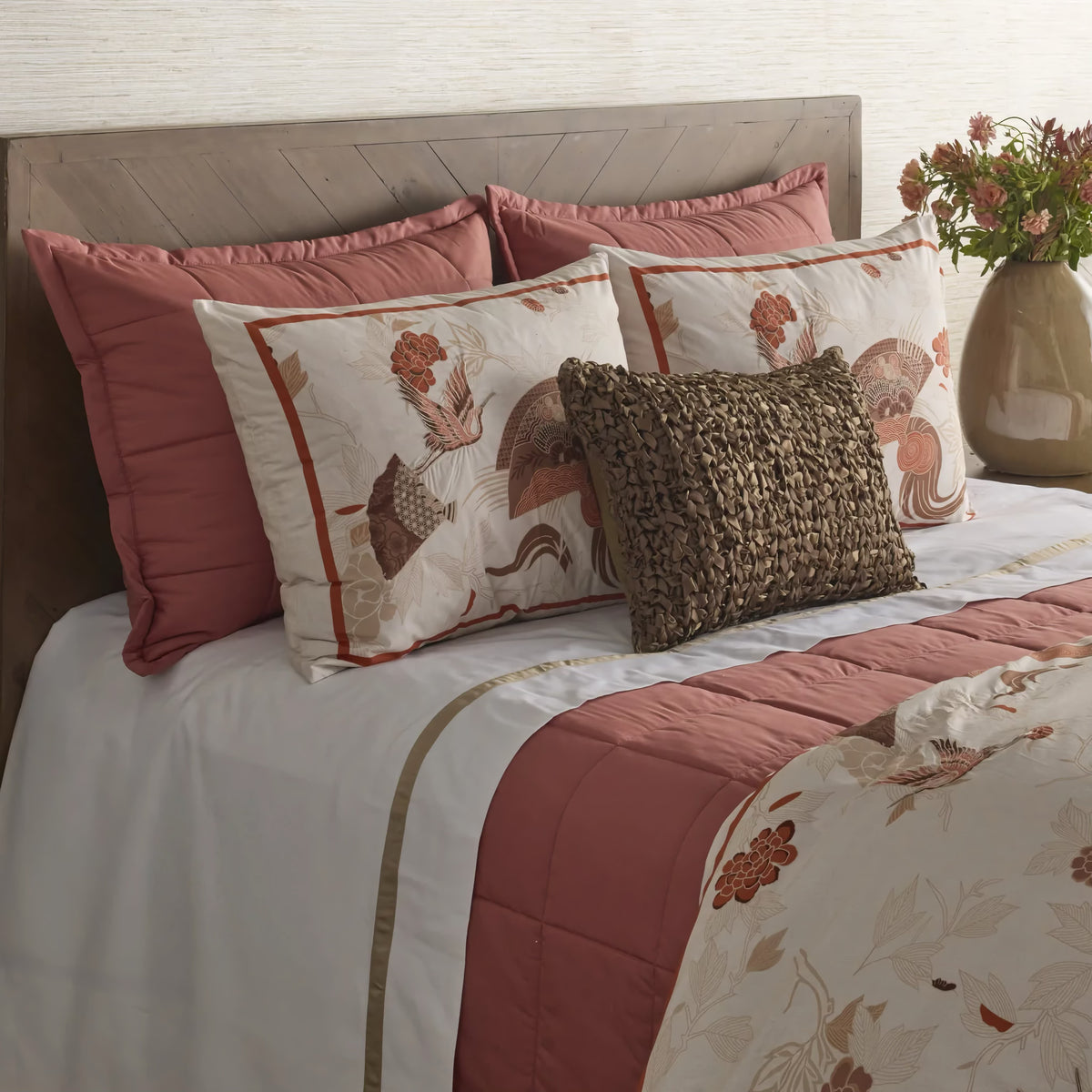 Bed with pink and cream bedding, floral pillows, and a Persimmon colored Ann Gish Slub Tencel Quilted Coverlet Set