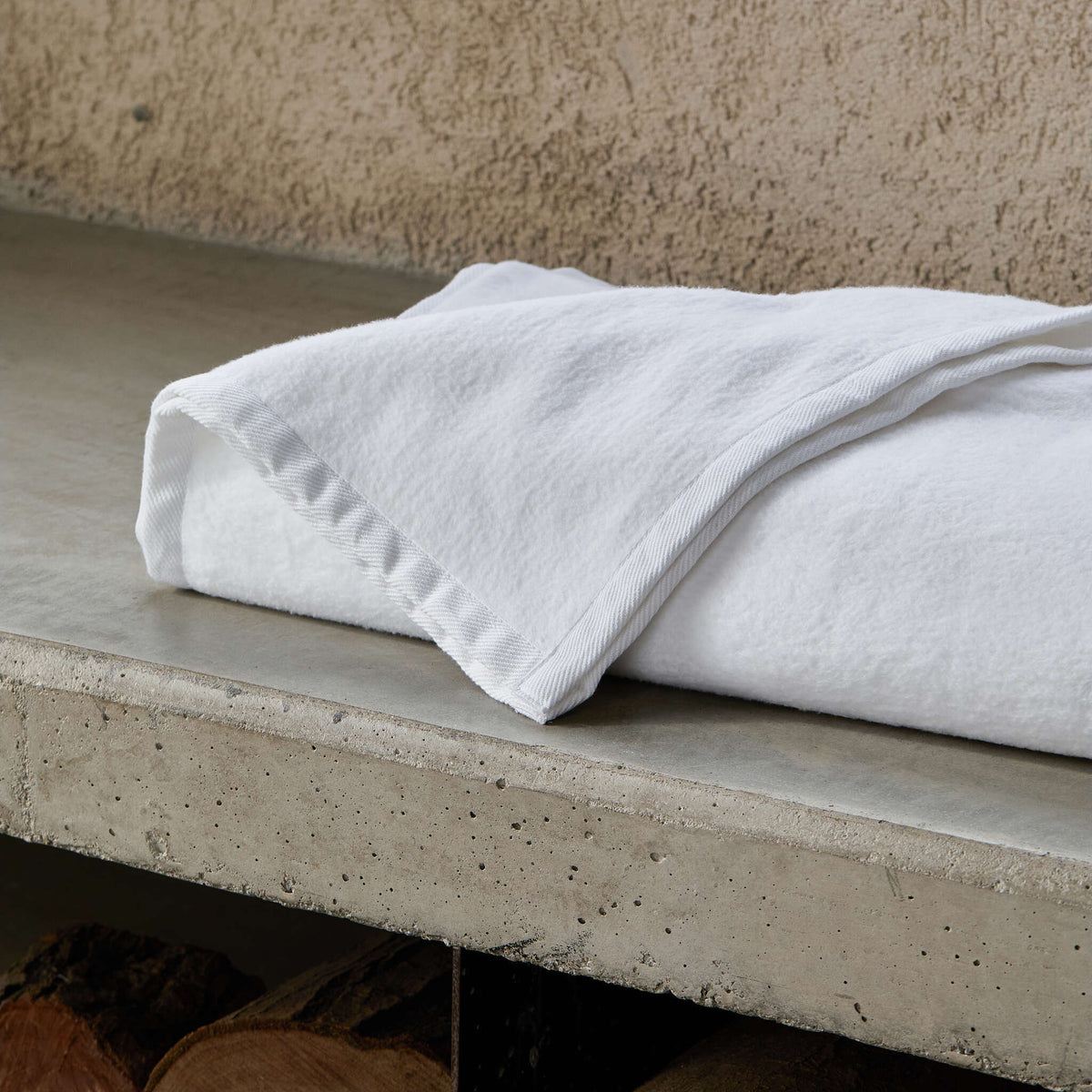 Folded white BOVI Finley Blanket on a concrete surface with a textured wall background