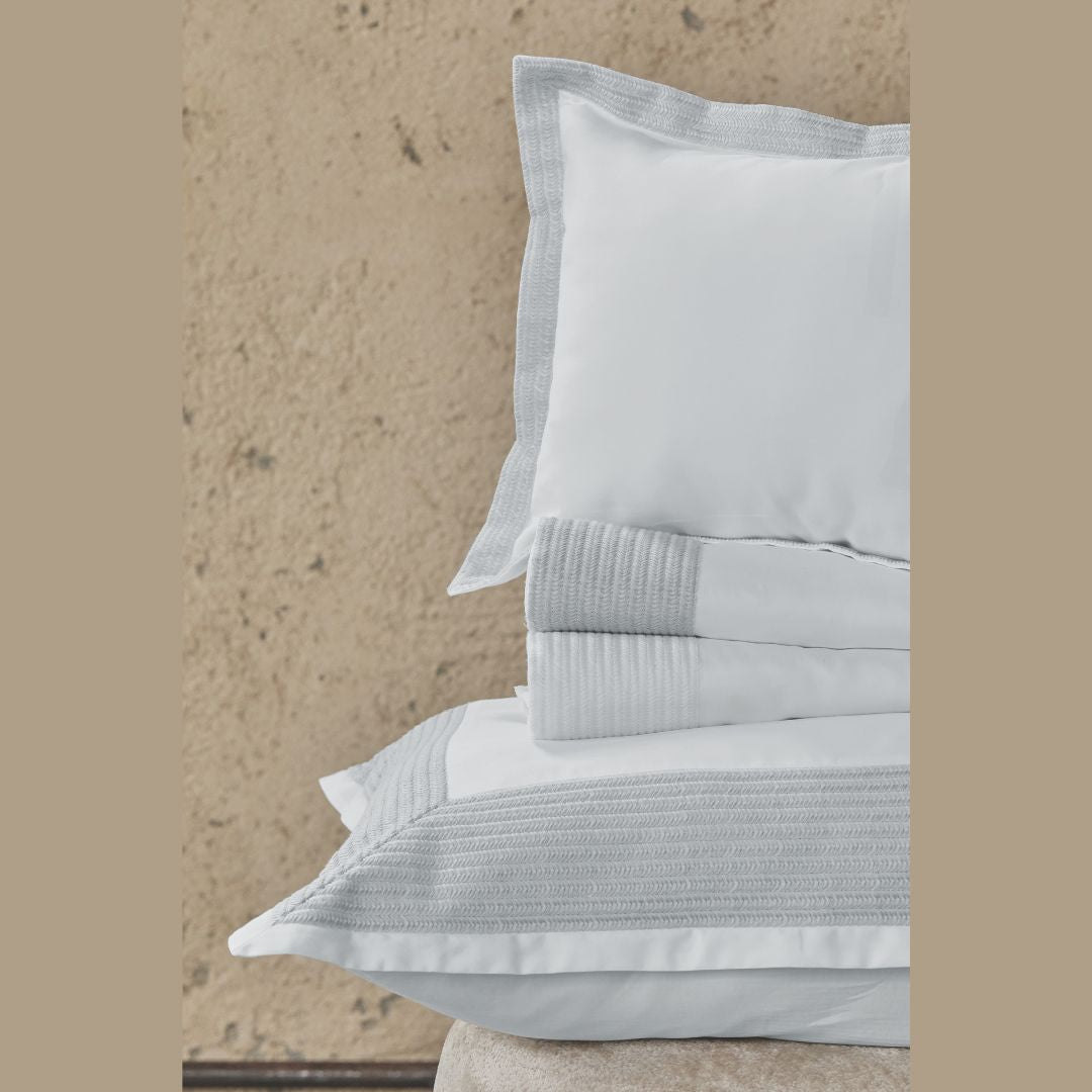 Stack of light gray bedding with textured edges against a beige stone wall.