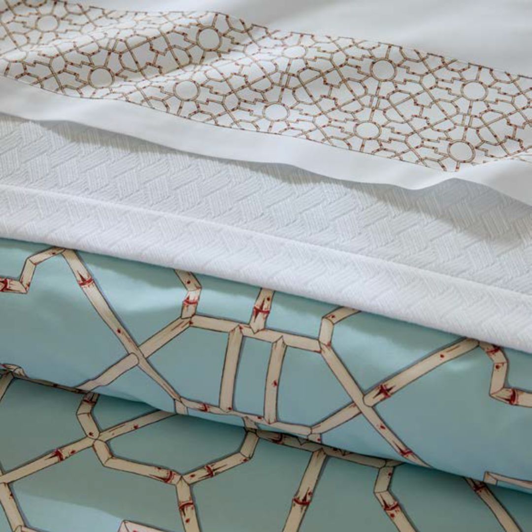Folded fabrics with geometric patterns evoke Italian luxury linens in white, brown, and light blue, stacked in a close-up view.