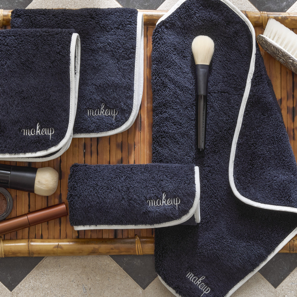 Set of Matouk Giza makeup towels with white edges on a wooden surface with make up tools and brush.