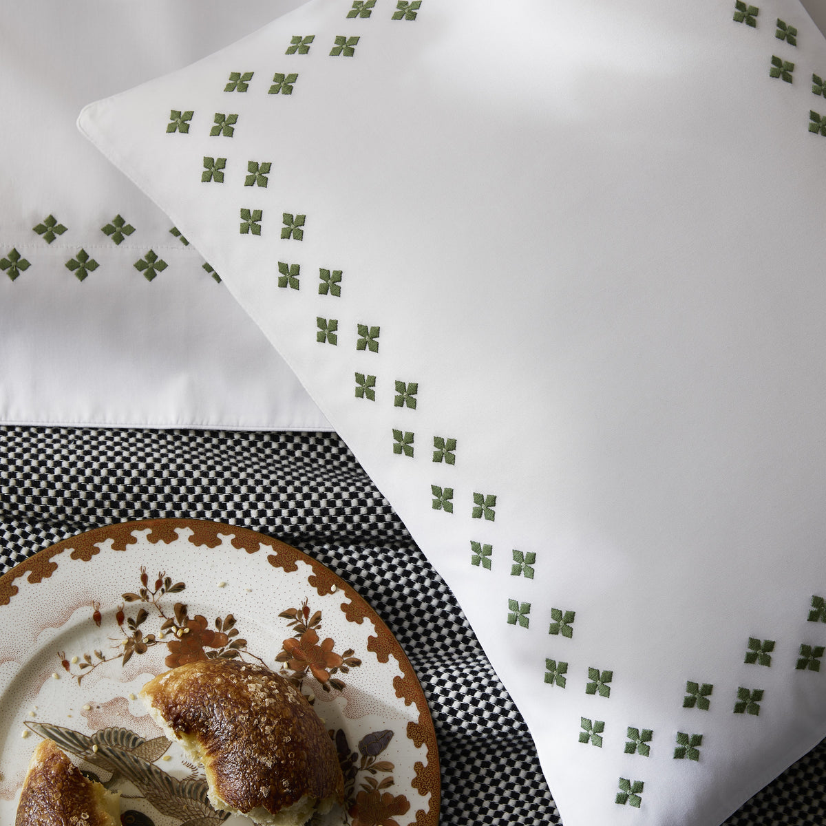 White pillow with green cross pattern, crafted from luxury percale bedding, next to bread on a checkered surface.