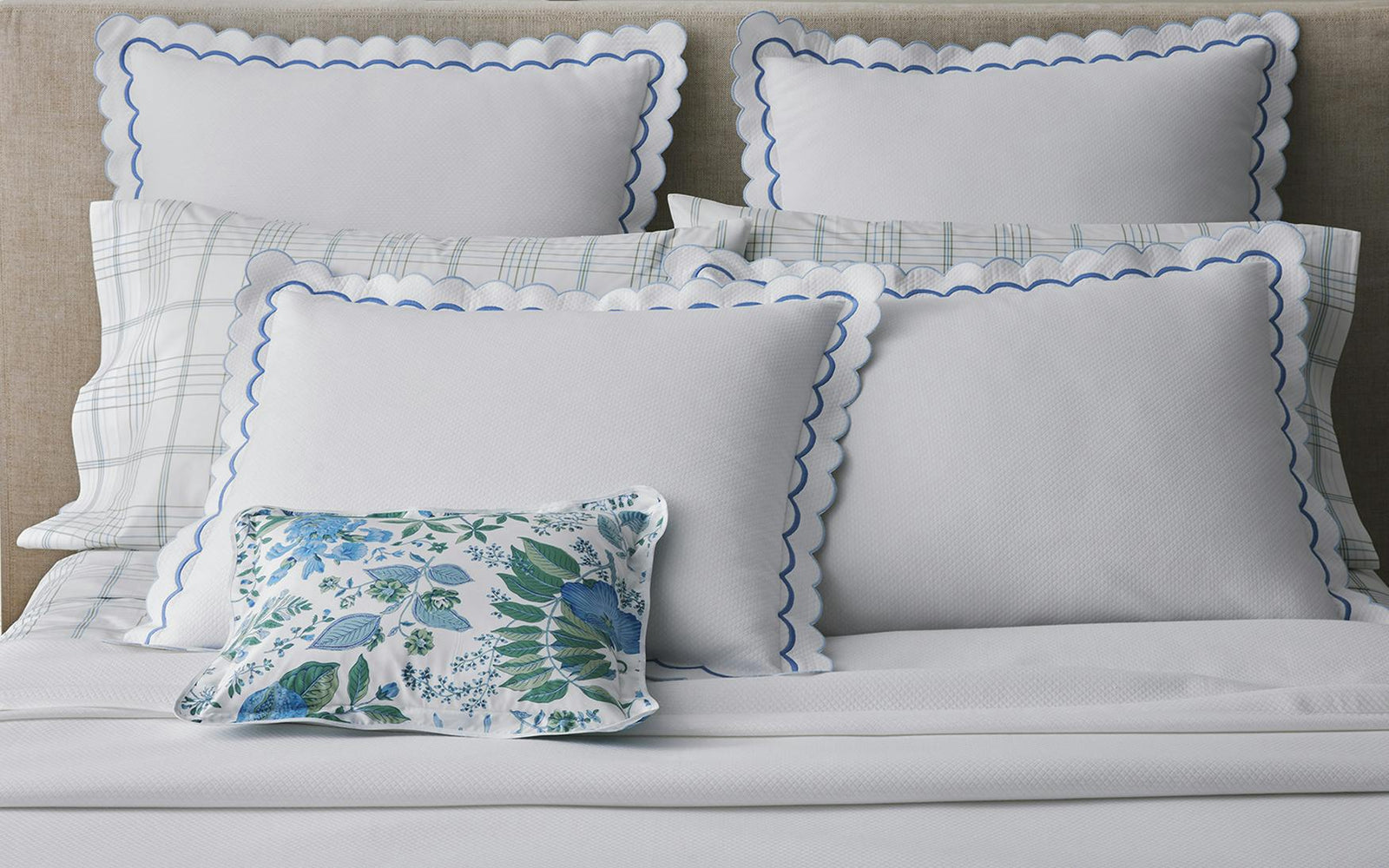 White pillows with blue scalloped edges are arranged on a bed, with a small floral pillow in front.