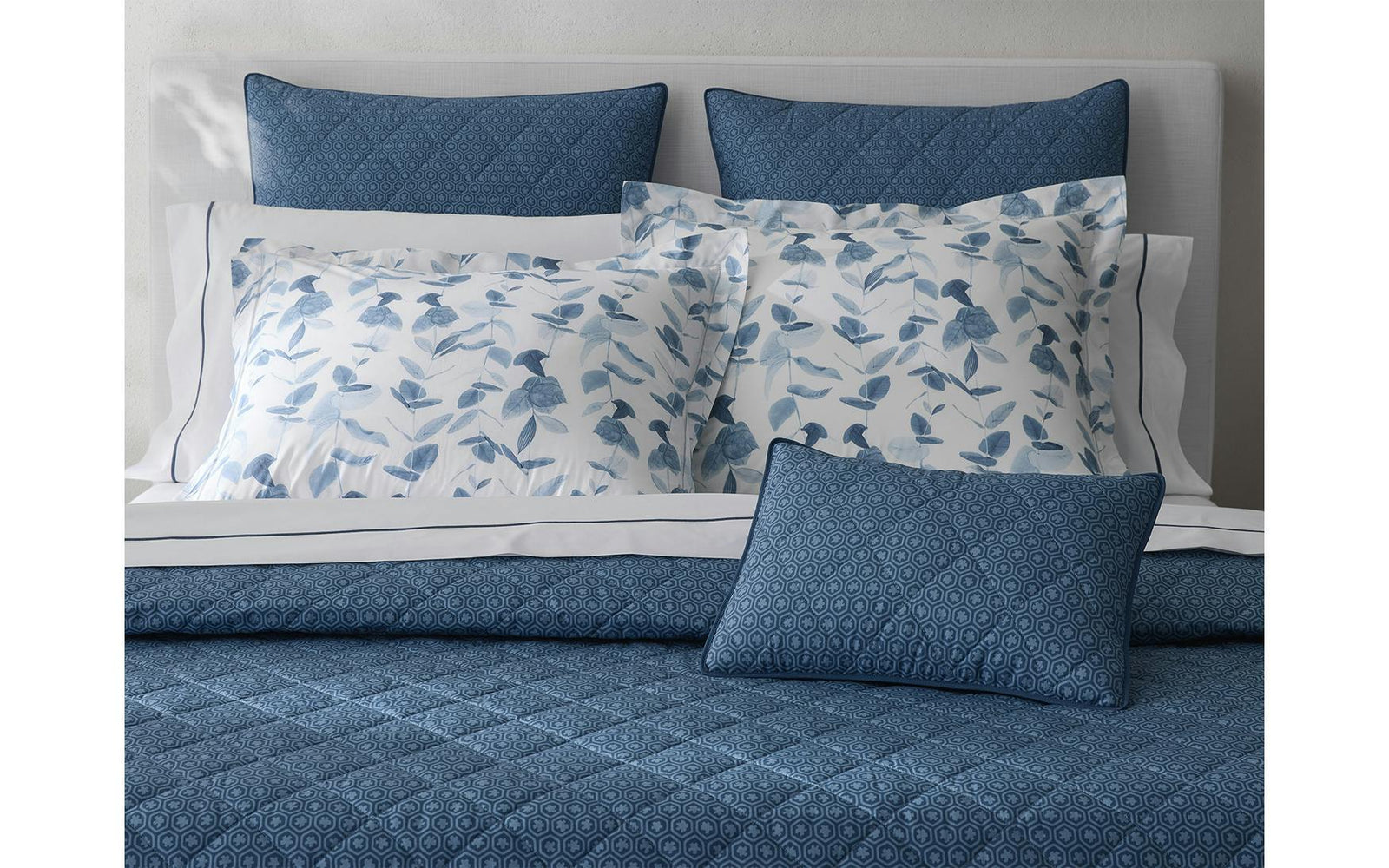 A neatly made bed with blue patterned pillows and quilt, and white pillowcases with a blue floral design.