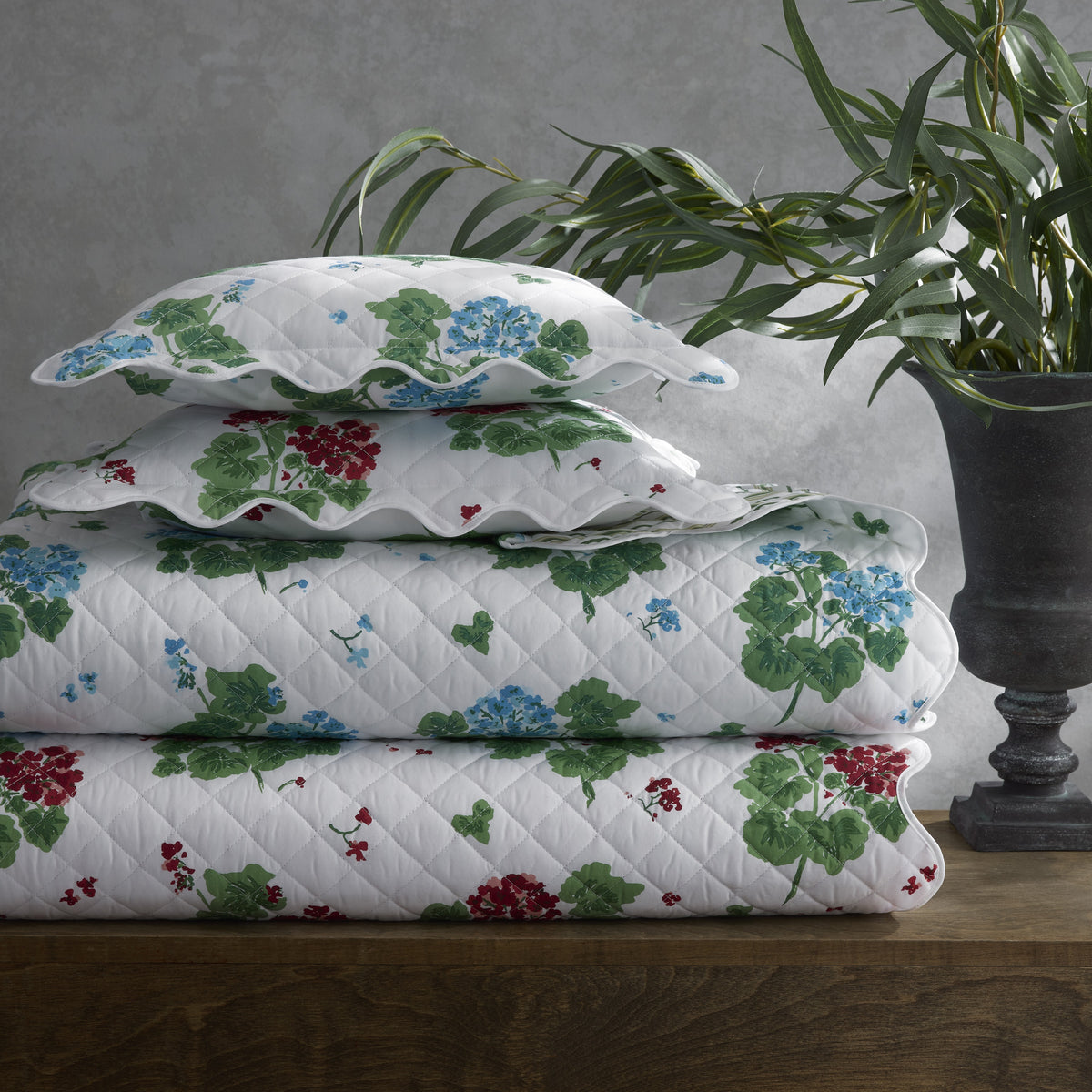Stack of floral-patterned quilts on a wooden surface with a plant in the background