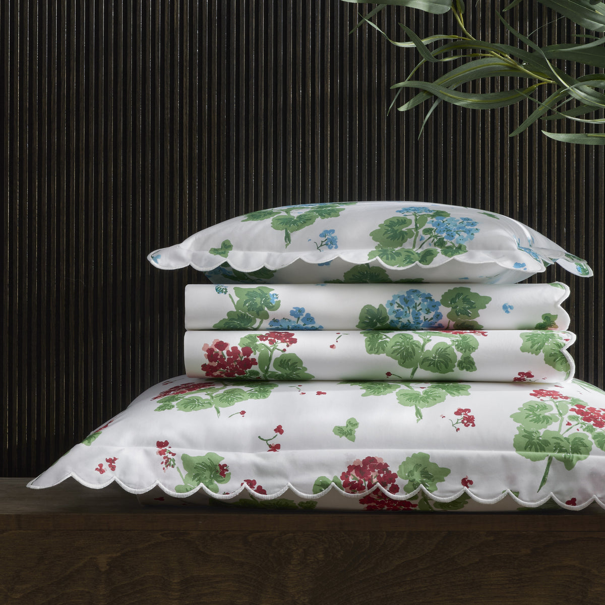 Stack of floral-patterned pillows on a dark surface with a plant in the background
