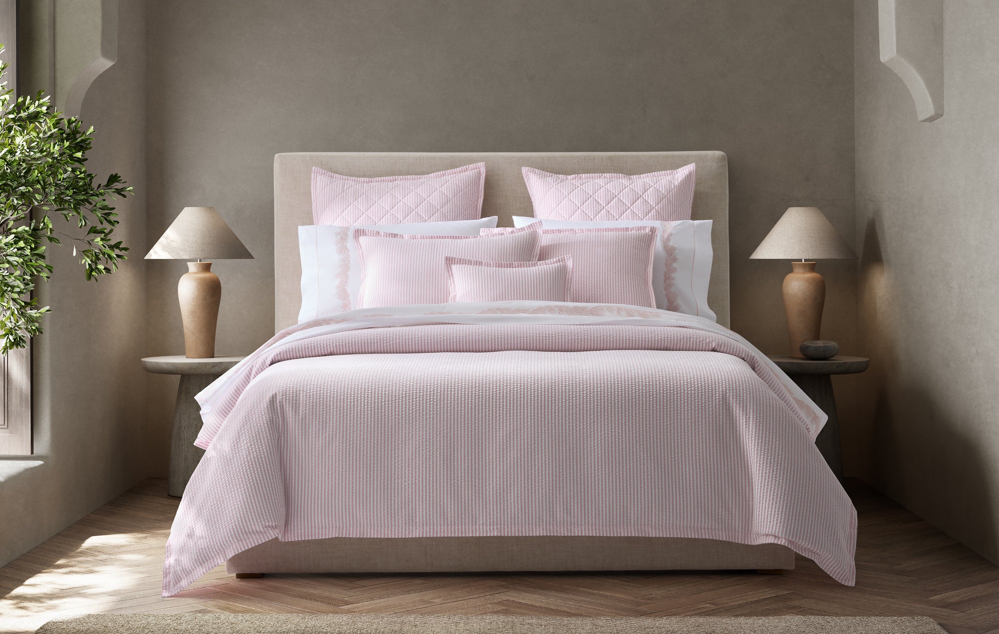 Bedroom with pink bedding and pillows on a bed, flanked by two lamps.