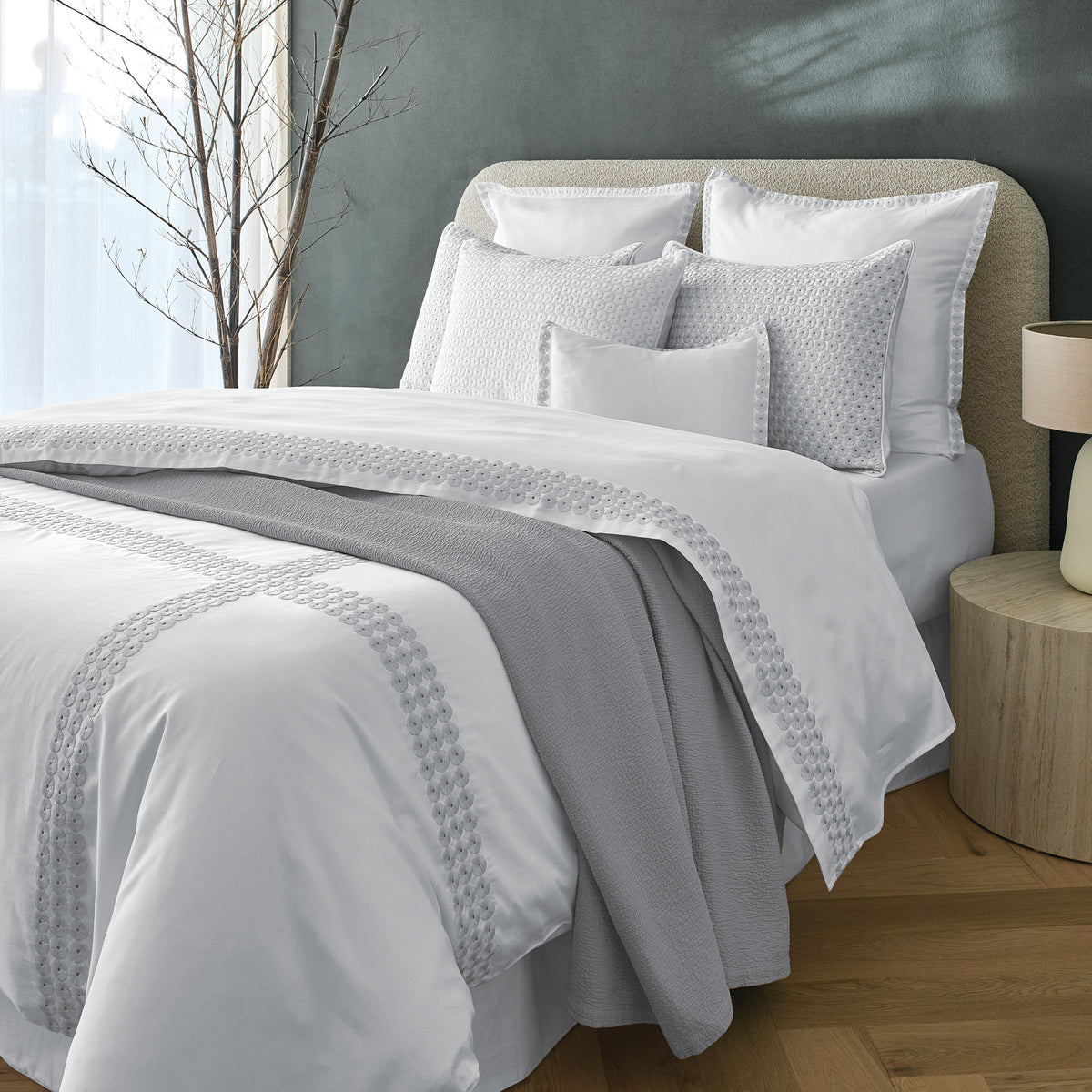 Neatly made bed with white bedding and gray throw blanket in a room with a green wall.