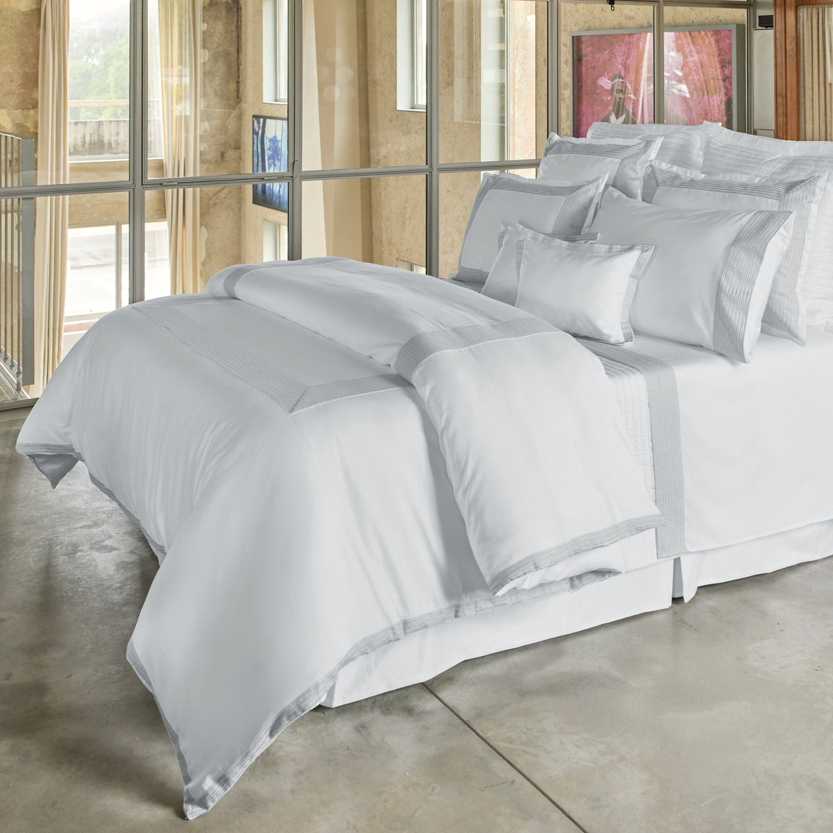 Gray bedding set on a bed in a room with large windows.
